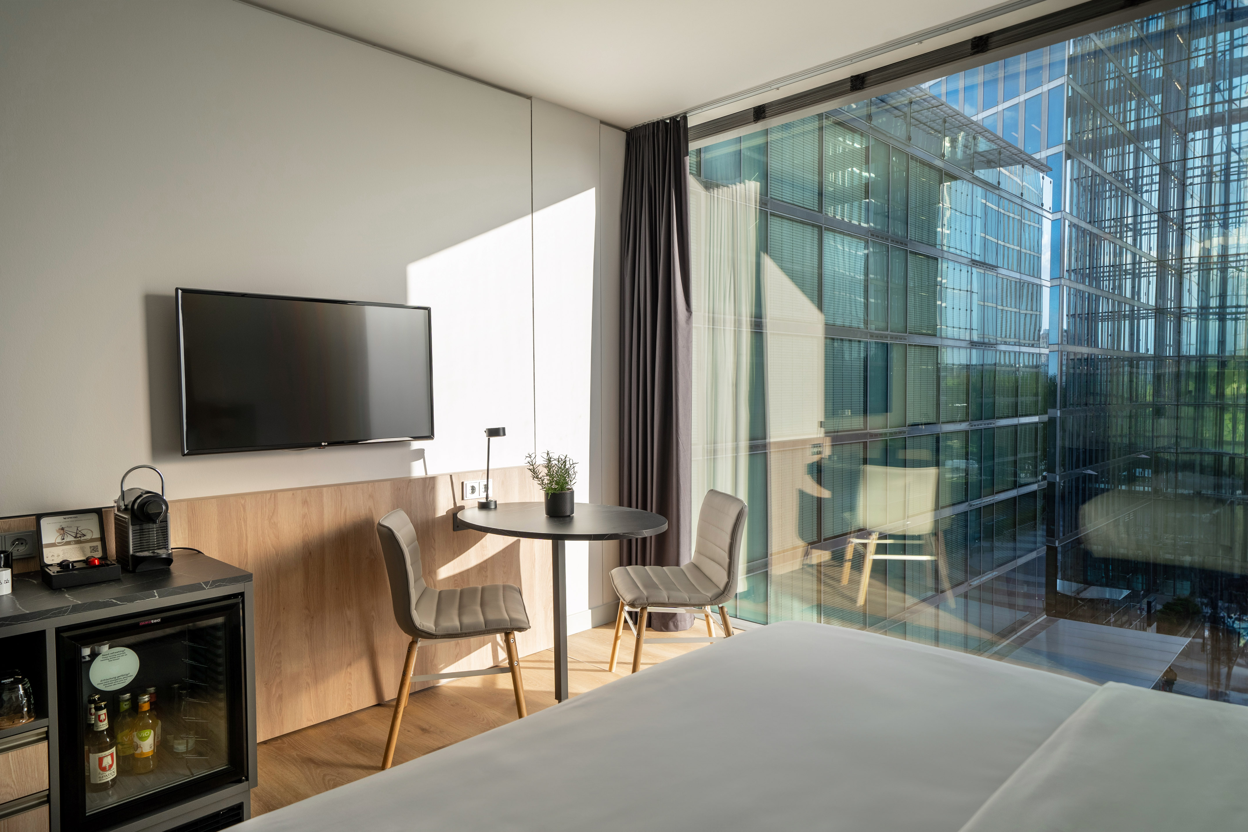 Modern hotel room with city view, floor-to-ceiling window, bed, and seating.