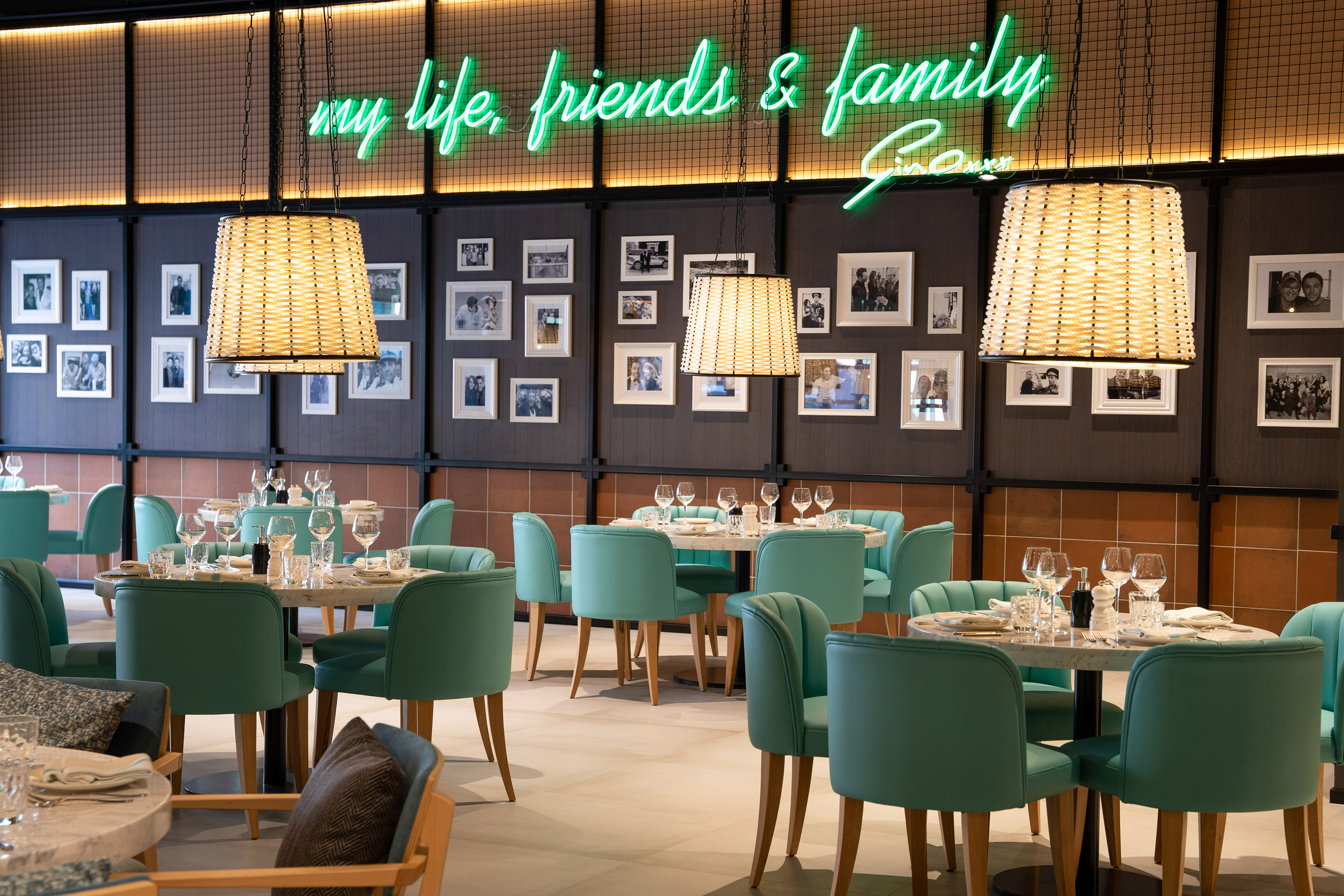 Restaurant interior with teal chairs, framed photo wall, and green neon sign.