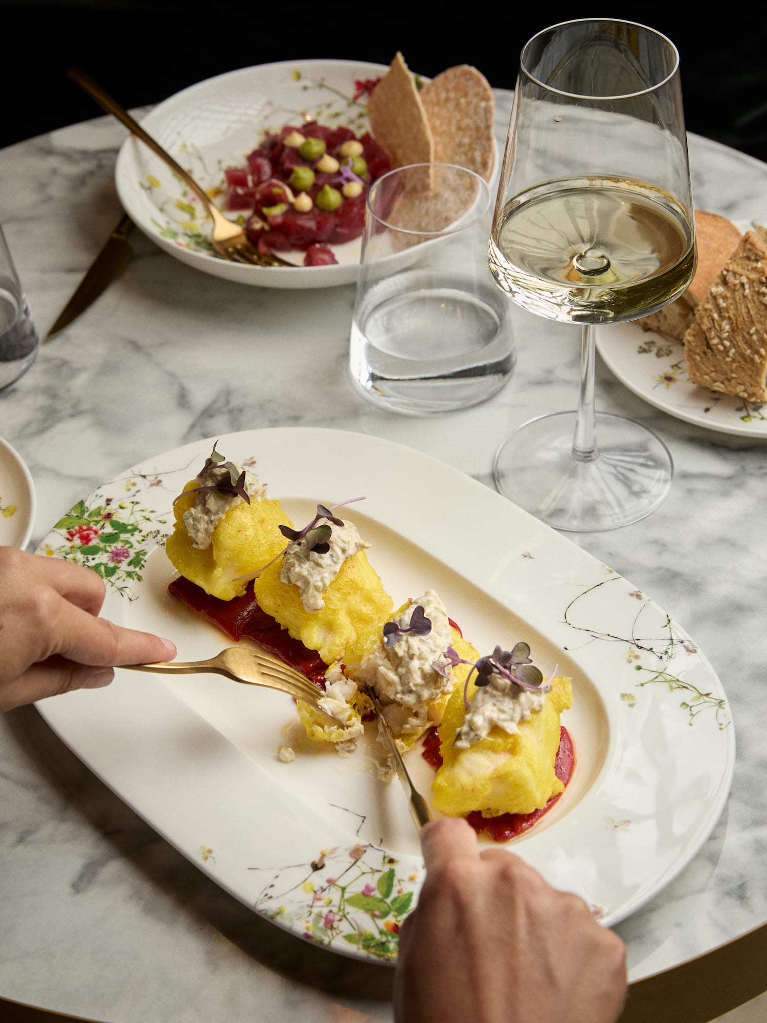 Battered fish with creamy sauce and beetroot, wine, tuna tartare on marble table.