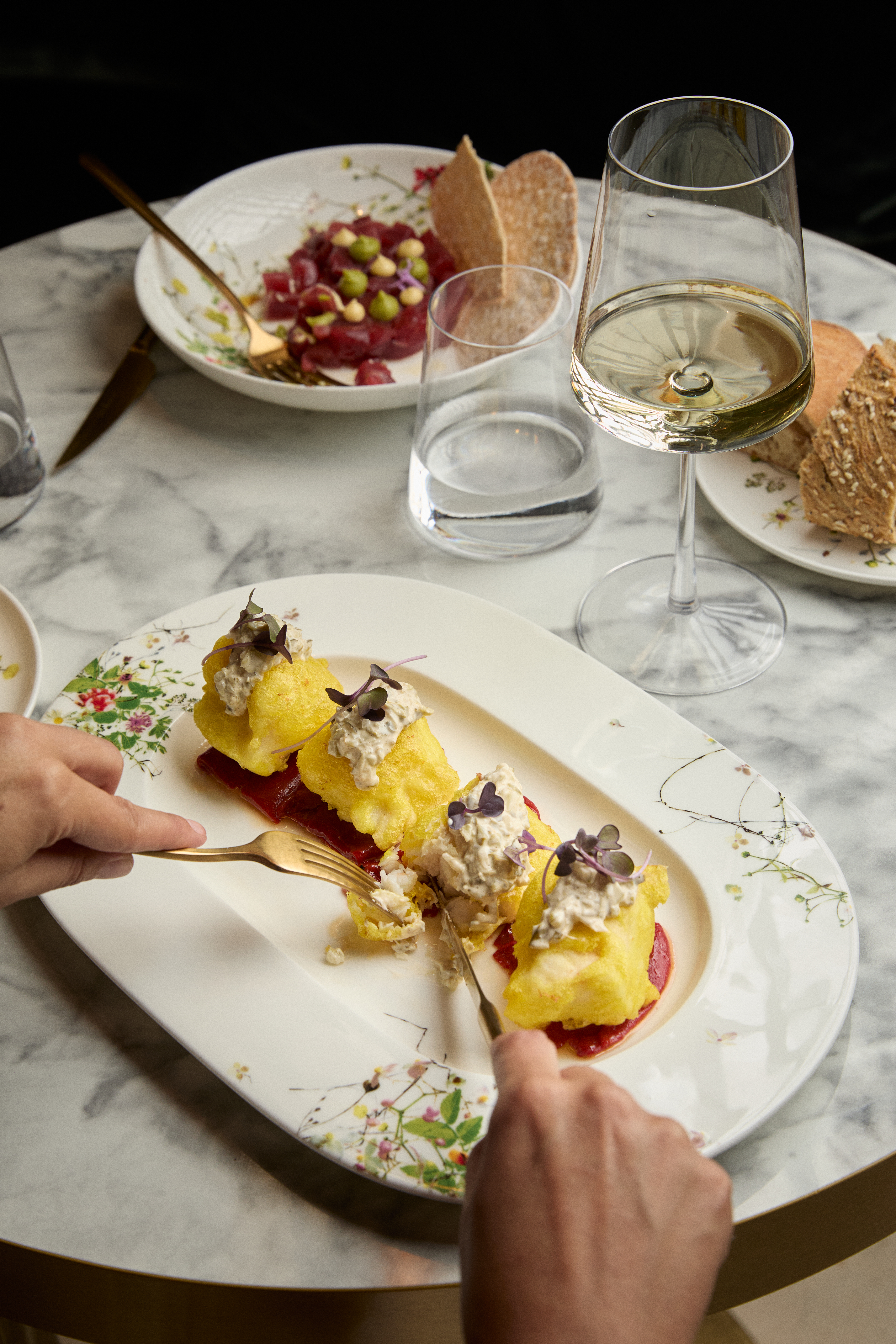 Battered fish with creamy sauce and beetroot, wine, tuna tartare on marble table.