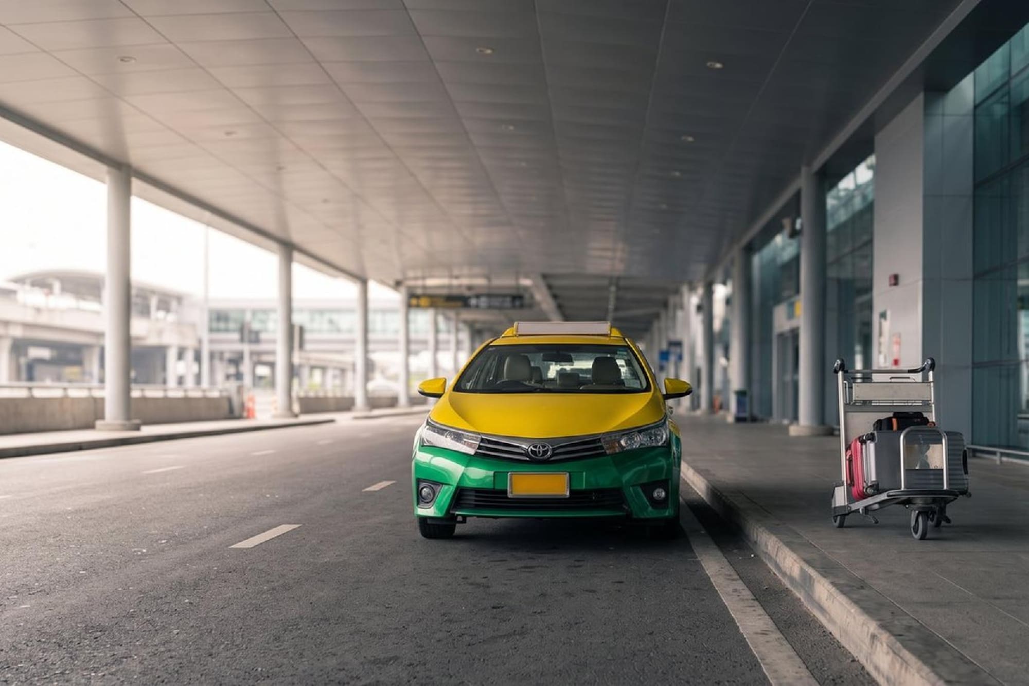 Yellow and green taxi car parked at an airport terminal with luggage cart.