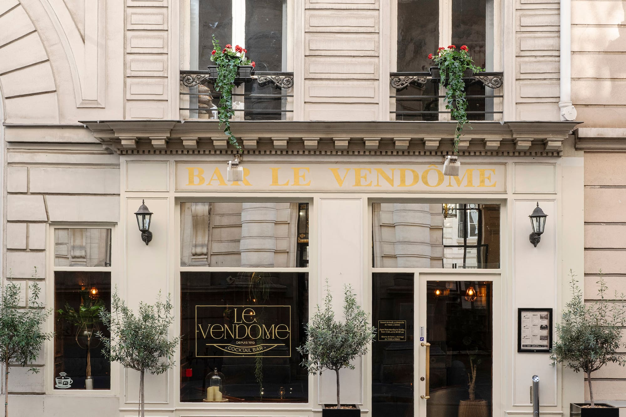 Bar Le Vendome Parisian cocktail bar facade with olive trees and ornate balconies.