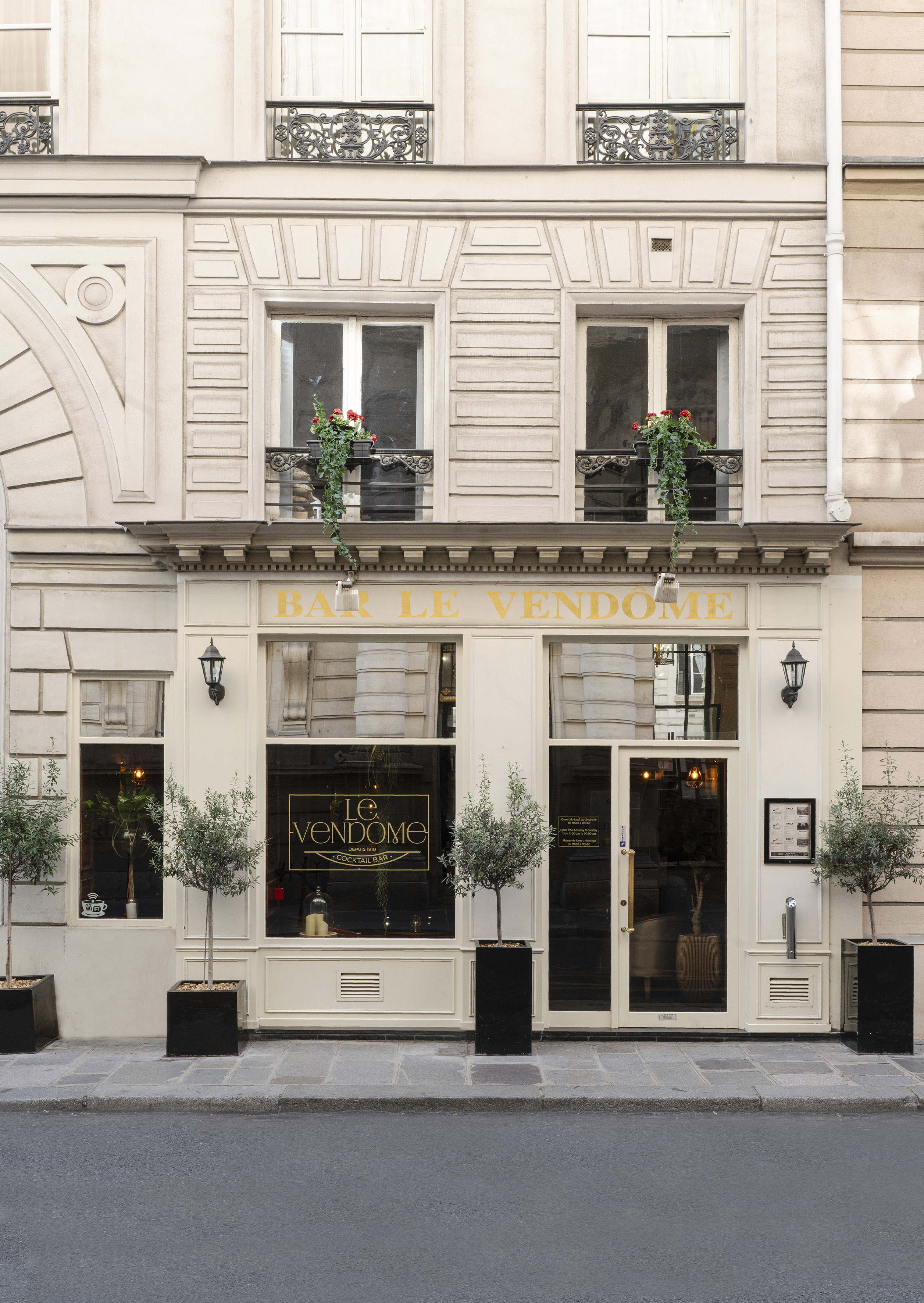 Bar Le Vendome Parisian cocktail bar facade with olive trees and ornate balconies.