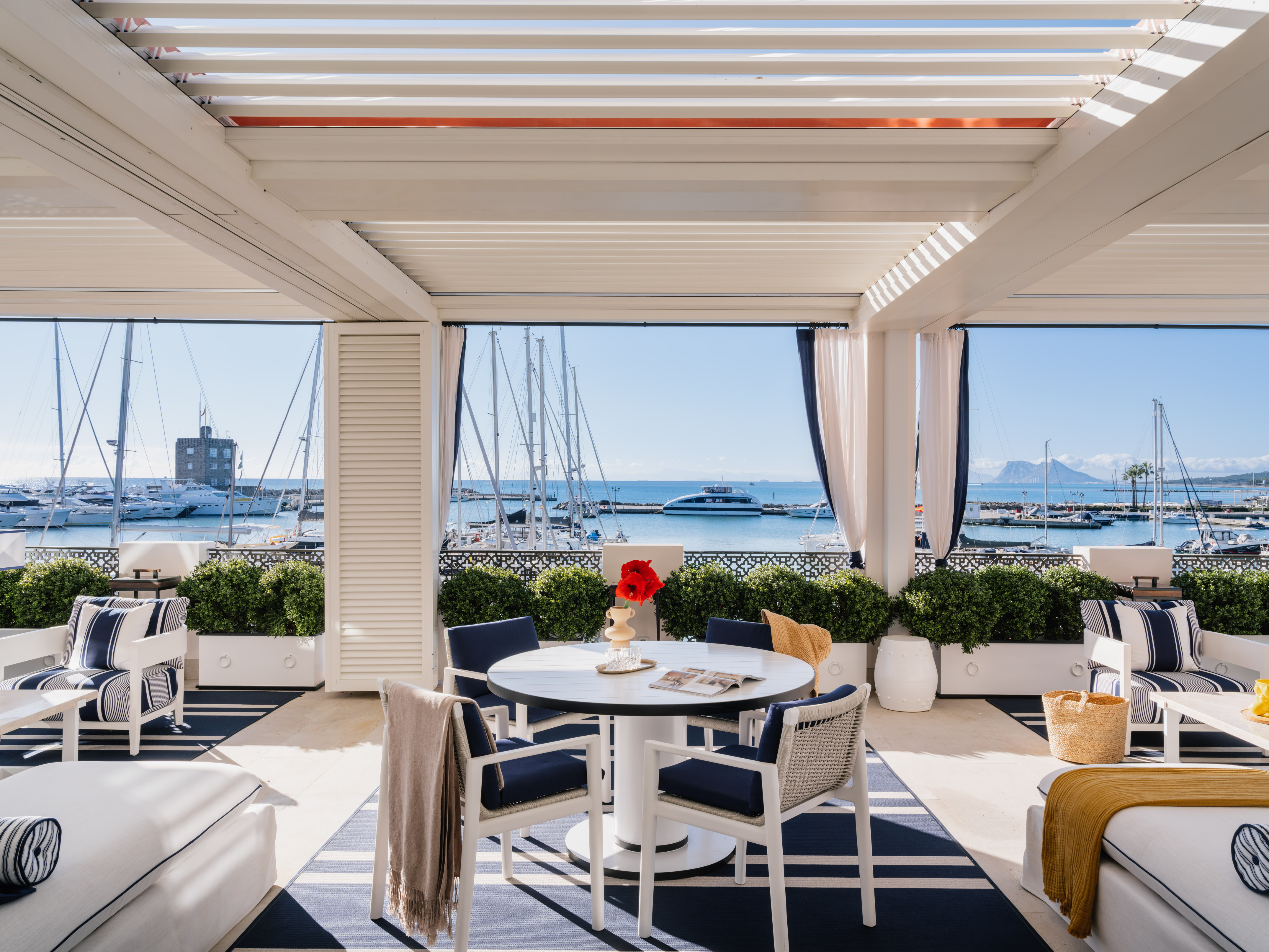 Patio with dining and lounge seating under pergola, overlooking yacht marina.