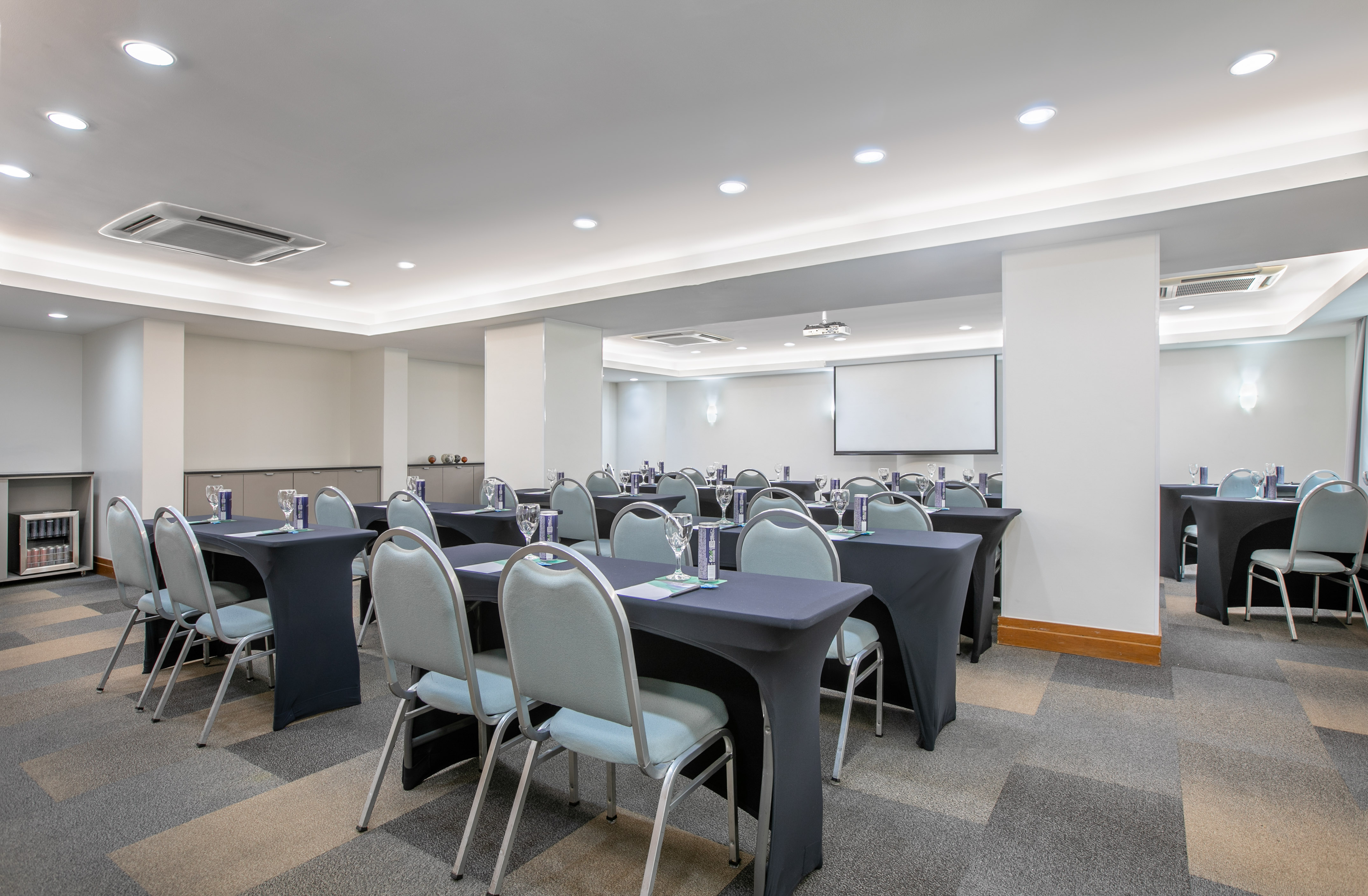Well-lit meeting room with black tables, light chairs, and a projector screen.