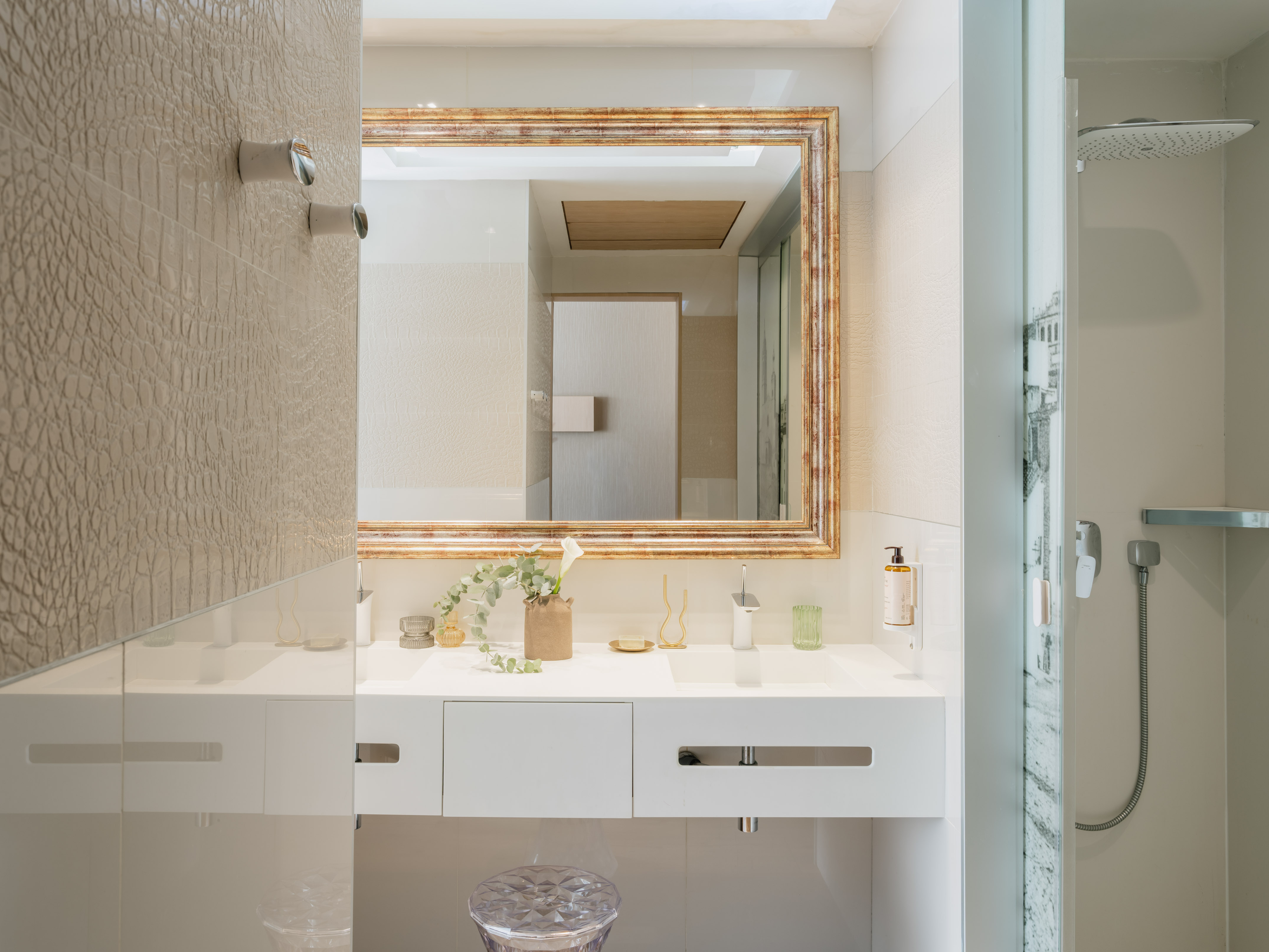 Modern bathroom with white vanity, ornate mirror, textured walls, and shower.