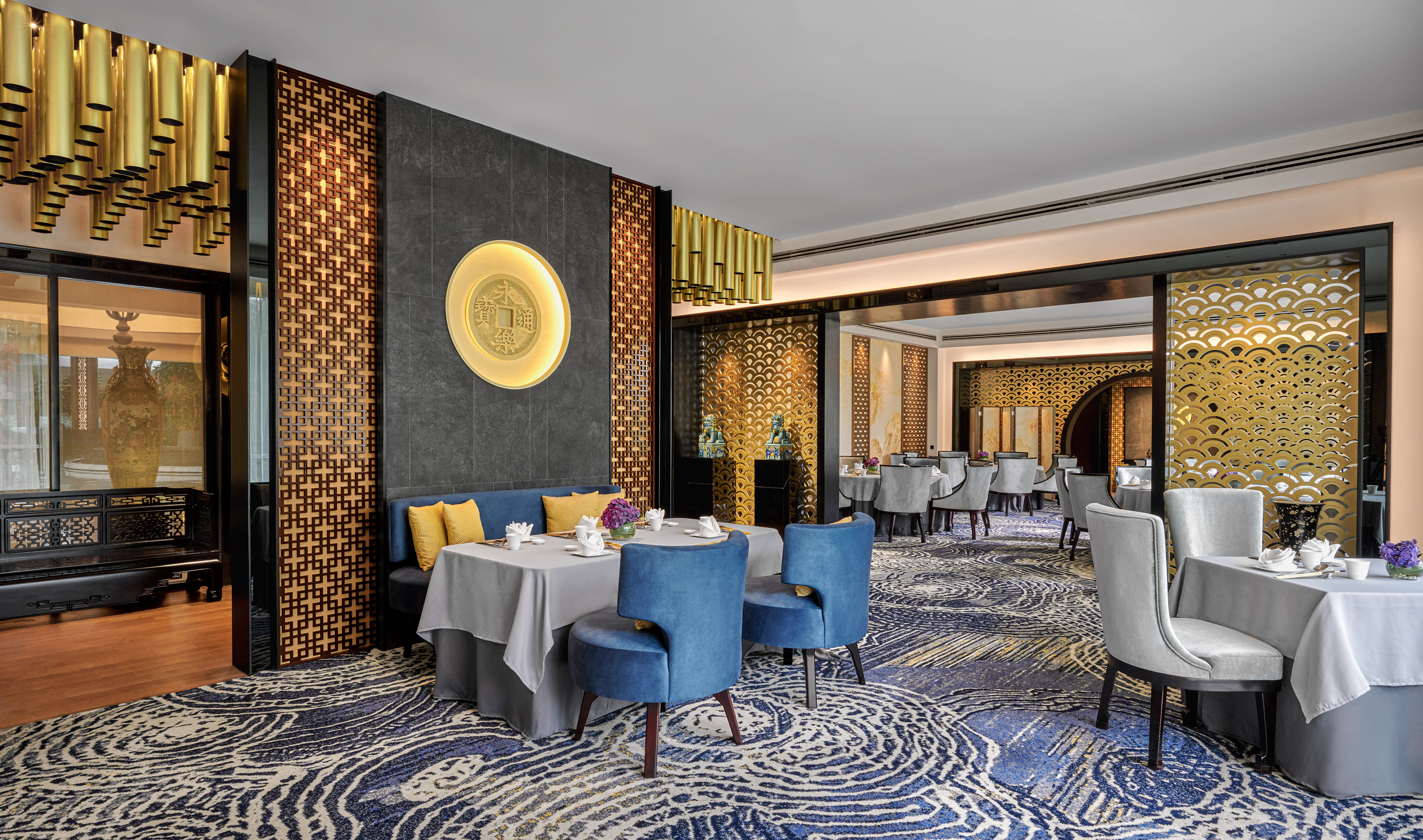 Elegant Chinese dining room with gold coin art, blue chairs, and ornate screens.
