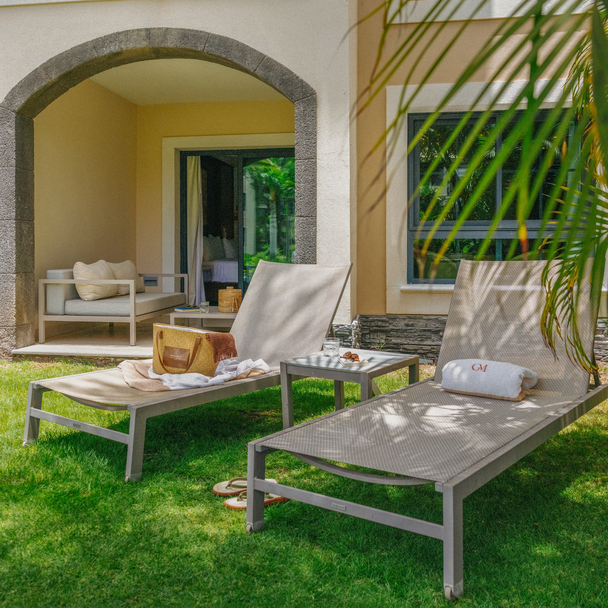 Tropical resort patio with lounge chairs, green lawn, and stone archway.