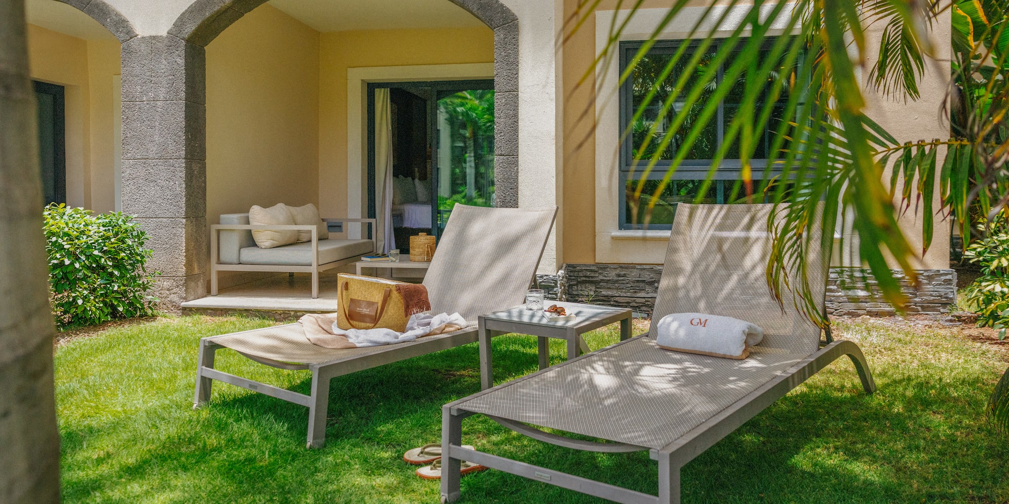 Tropical resort patio with lounge chairs, green lawn, and stone archway.