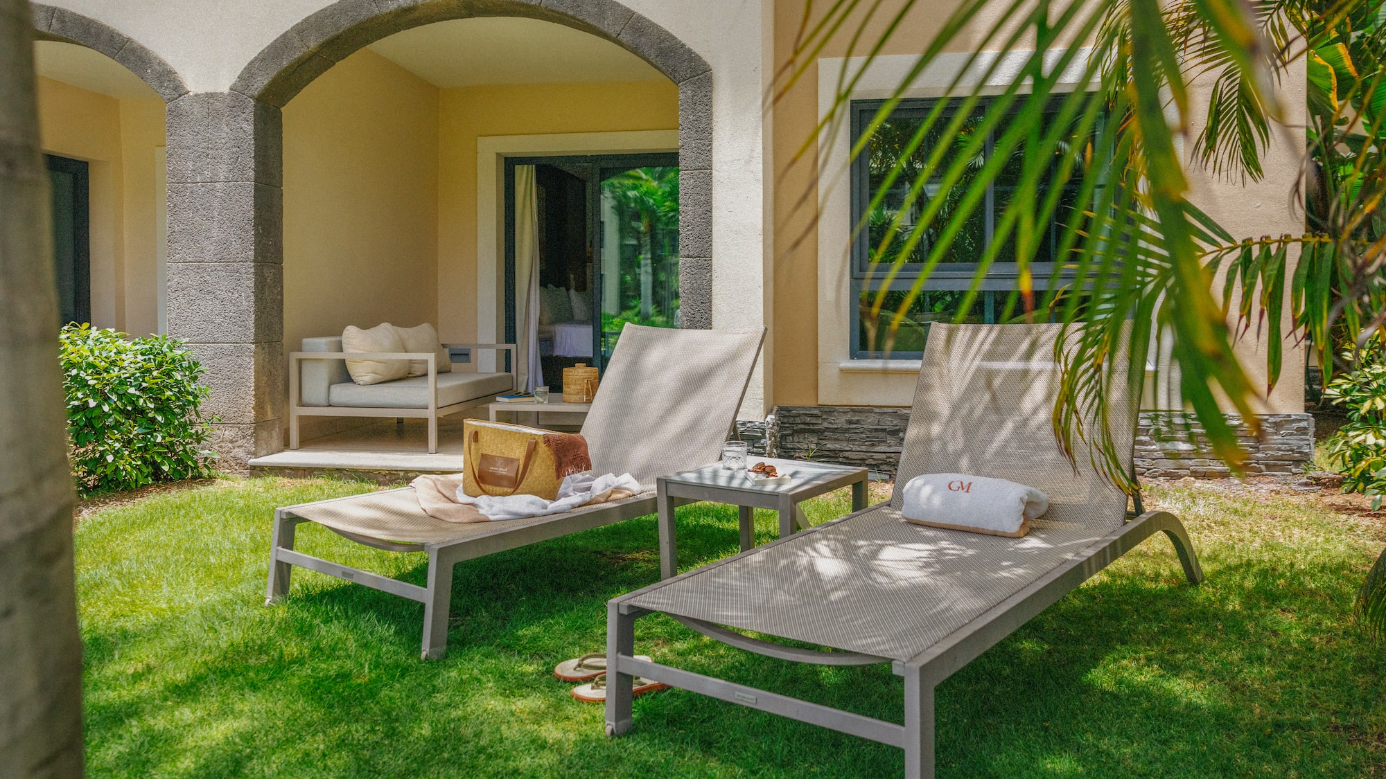 Tropical resort patio with lounge chairs, green lawn, and stone archway.