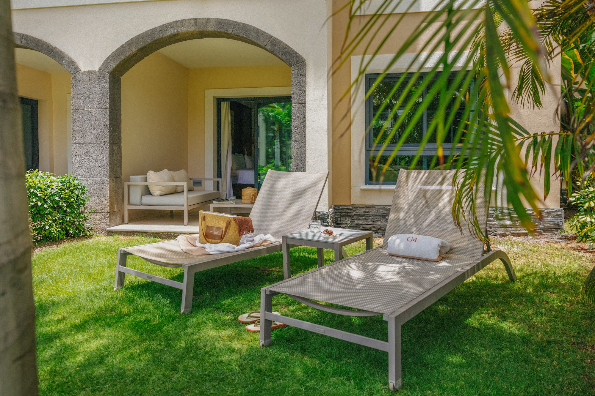 Tropical resort patio with lounge chairs, green lawn, and stone archway.