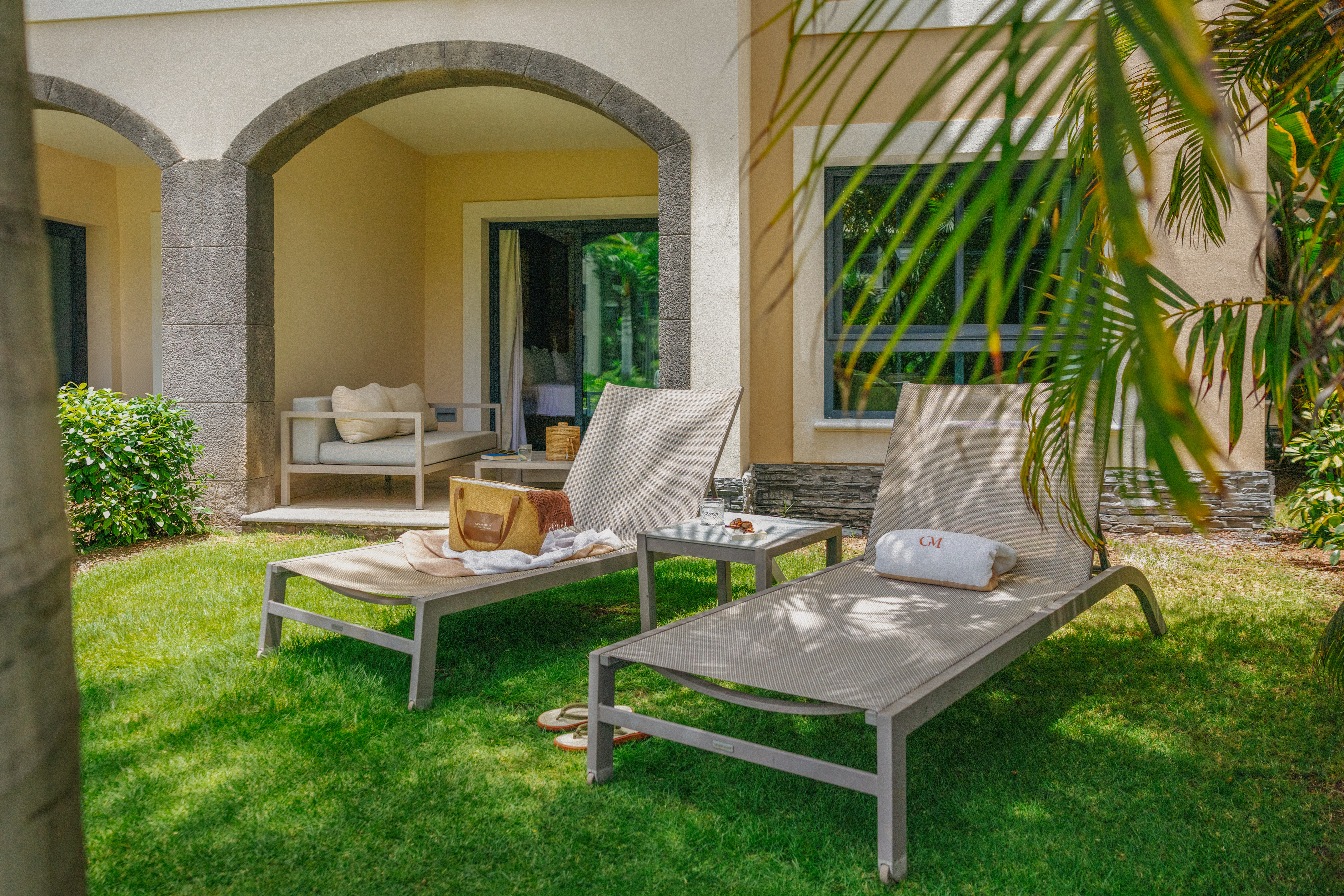 Tropical resort patio with lounge chairs, green lawn, and stone archway.