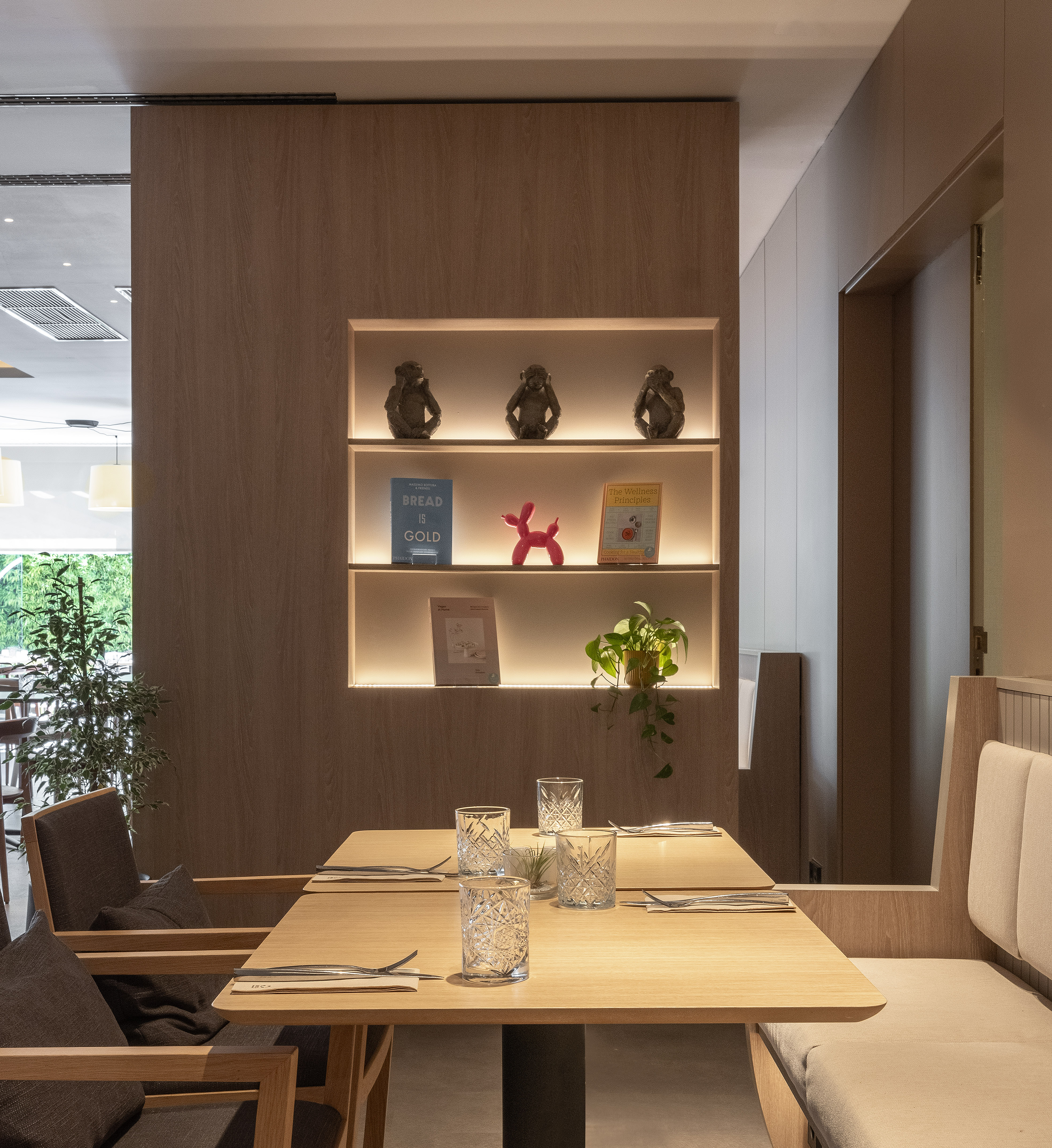 Modern dining area with wooden tables, booth seating, and illuminated decor shelves.