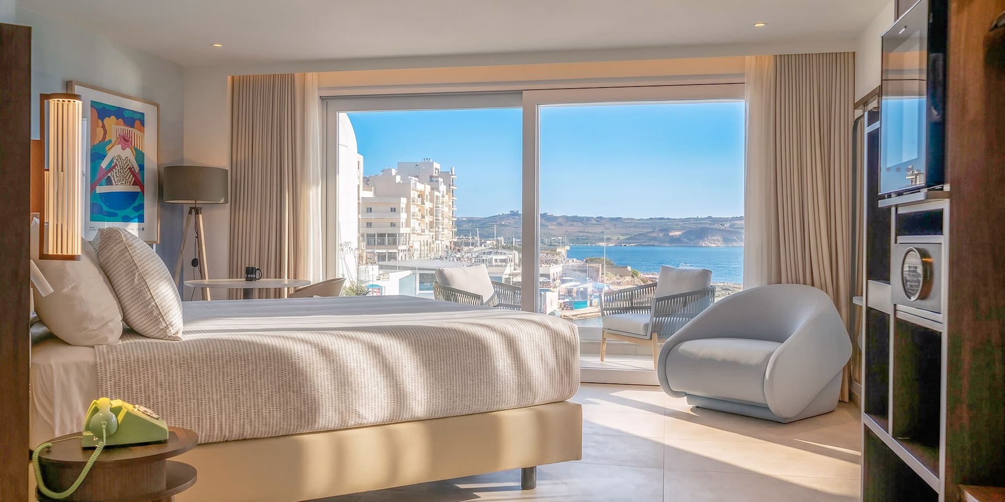 Modern Malta hotel room with sea view, comfortable bed, and balcony.