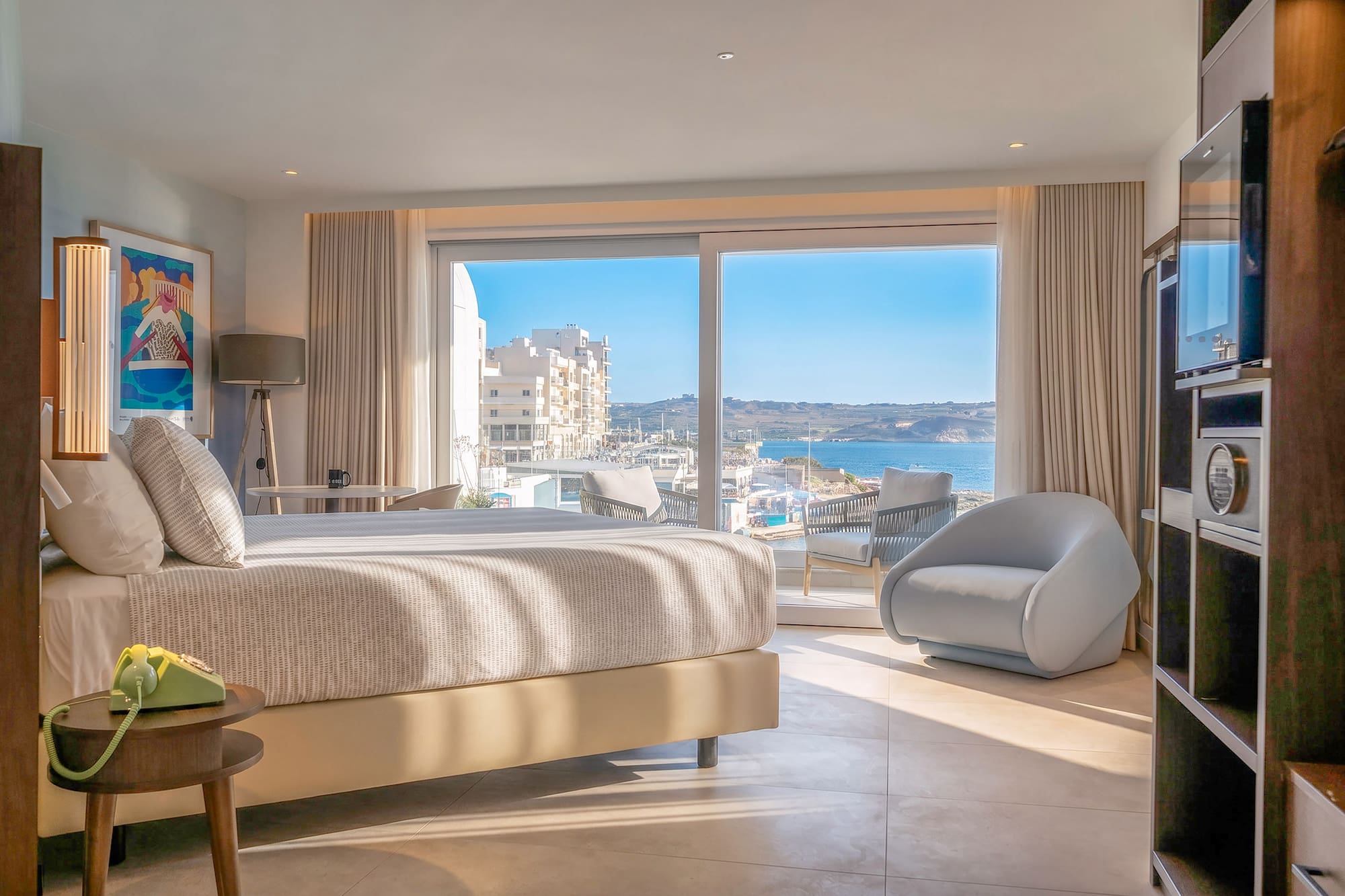 Modern Malta hotel room with sea view, comfortable bed, and balcony.