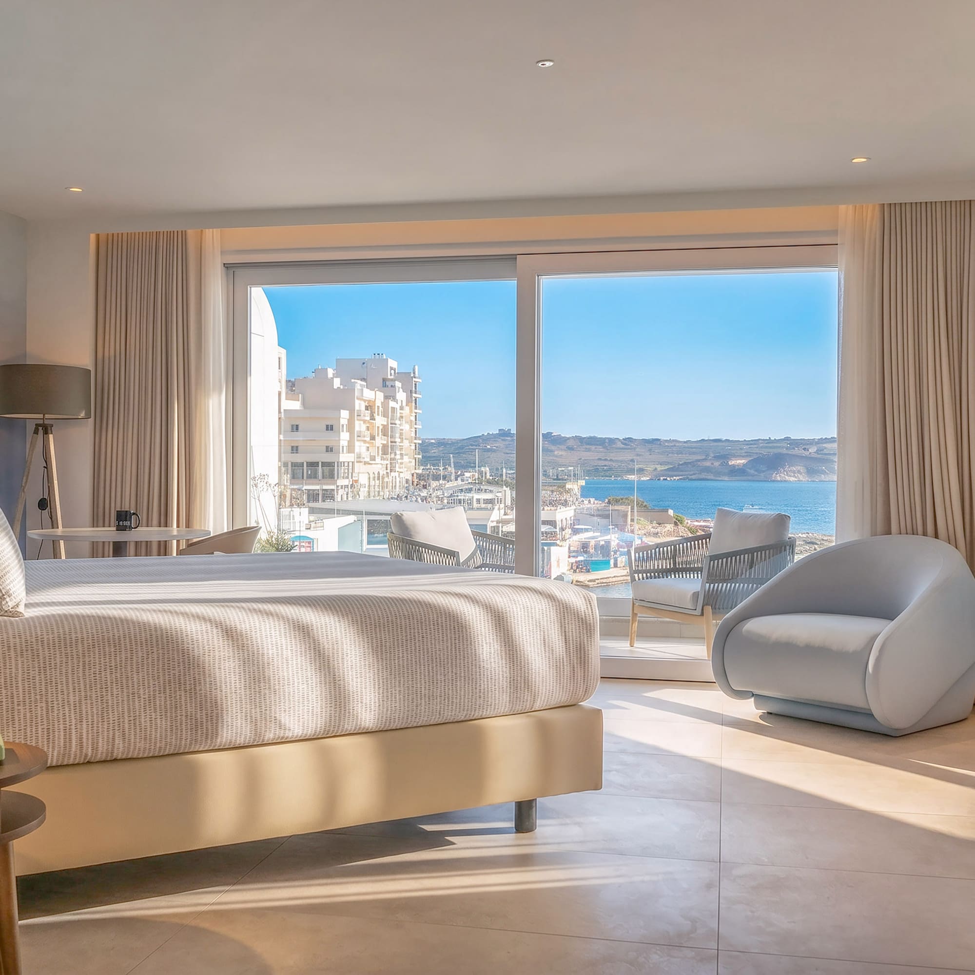 Modern hotel bedroom with sea view balcony, bed, and armchair.