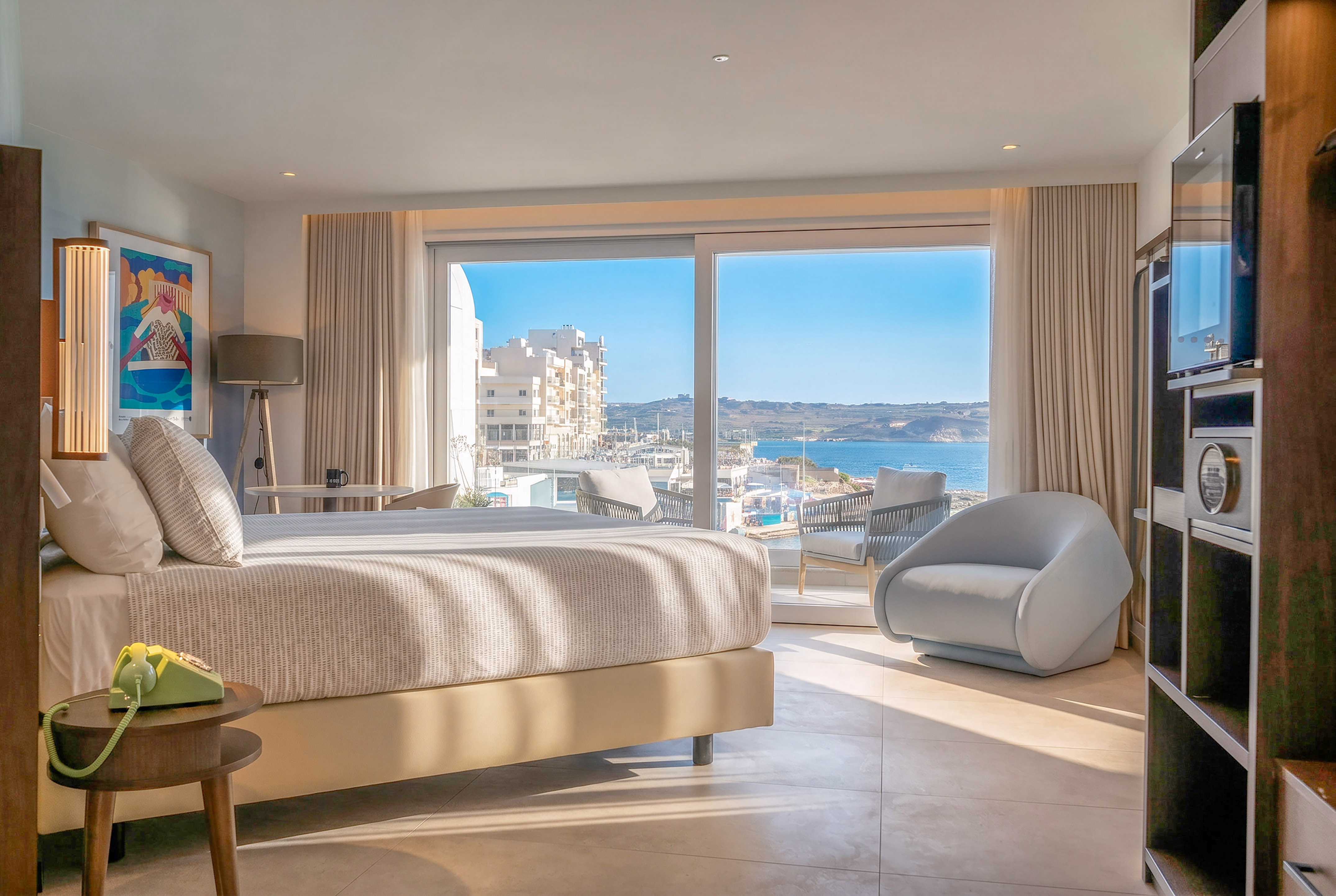 Sunny hotel bedroom with Mediterranean sea view, large bed, and balcony.