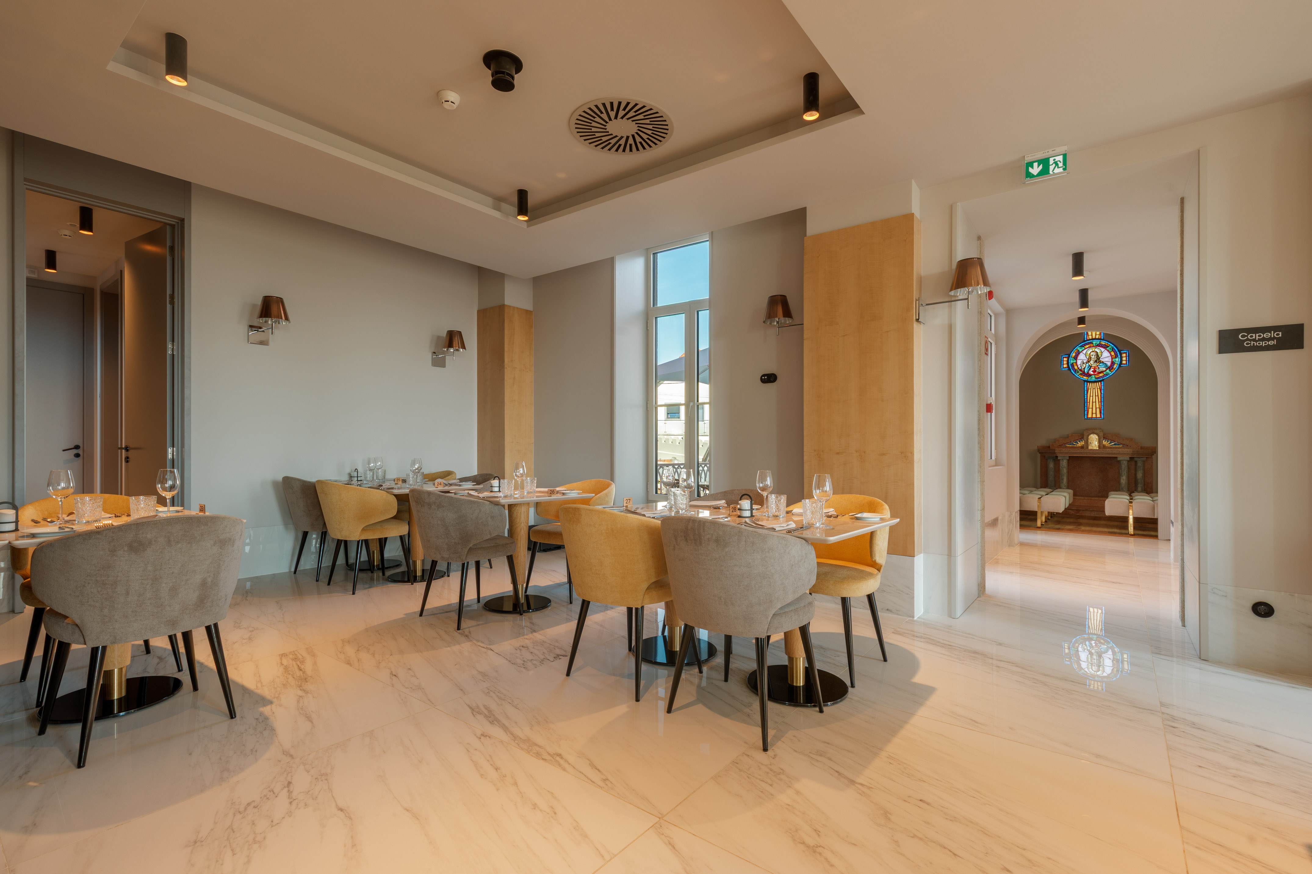 Modern restaurant interior with set tables, marble floor, and chapel view.