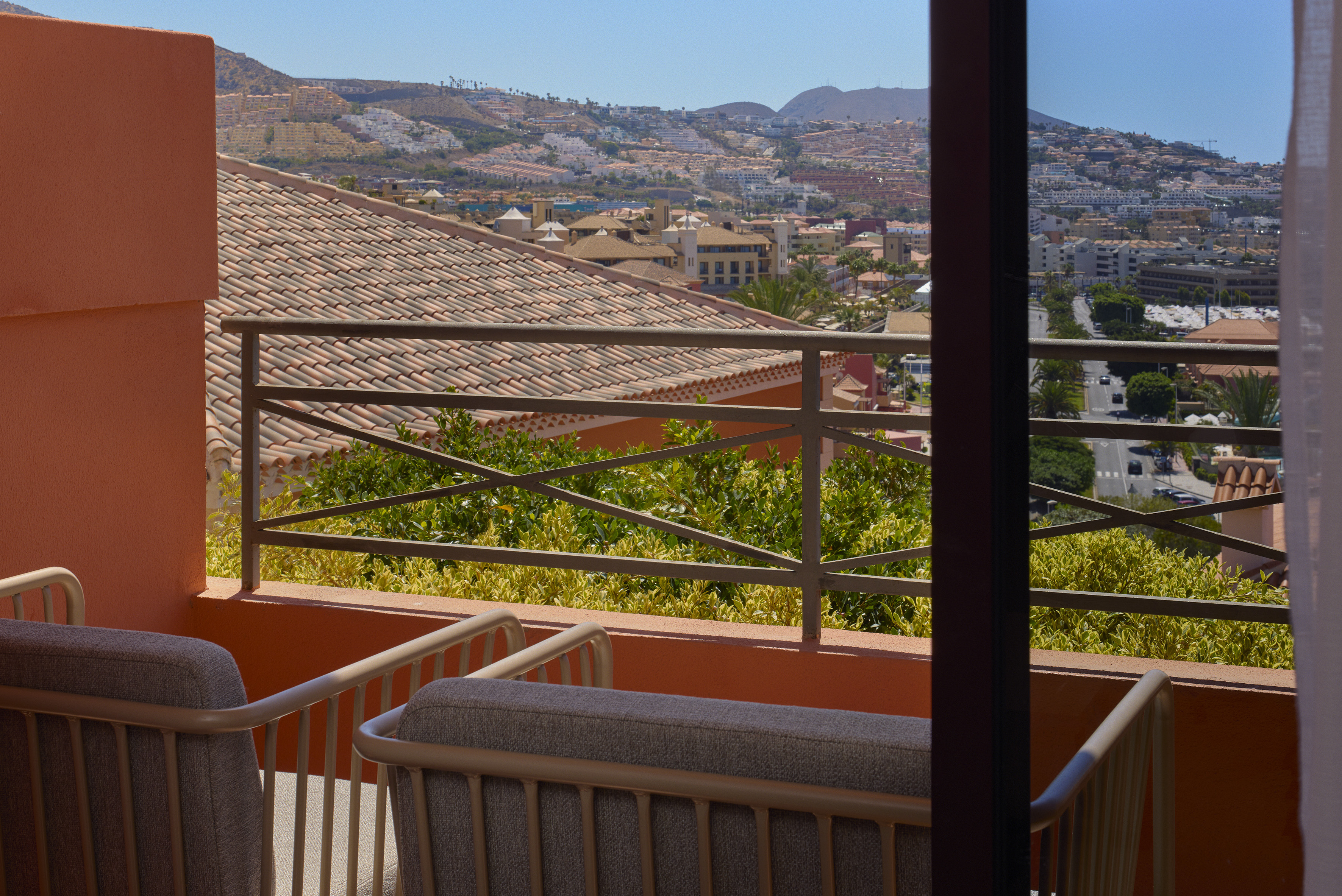 Hotel balcony with chairs, terracotta walls, overlooking a sunny resort town.