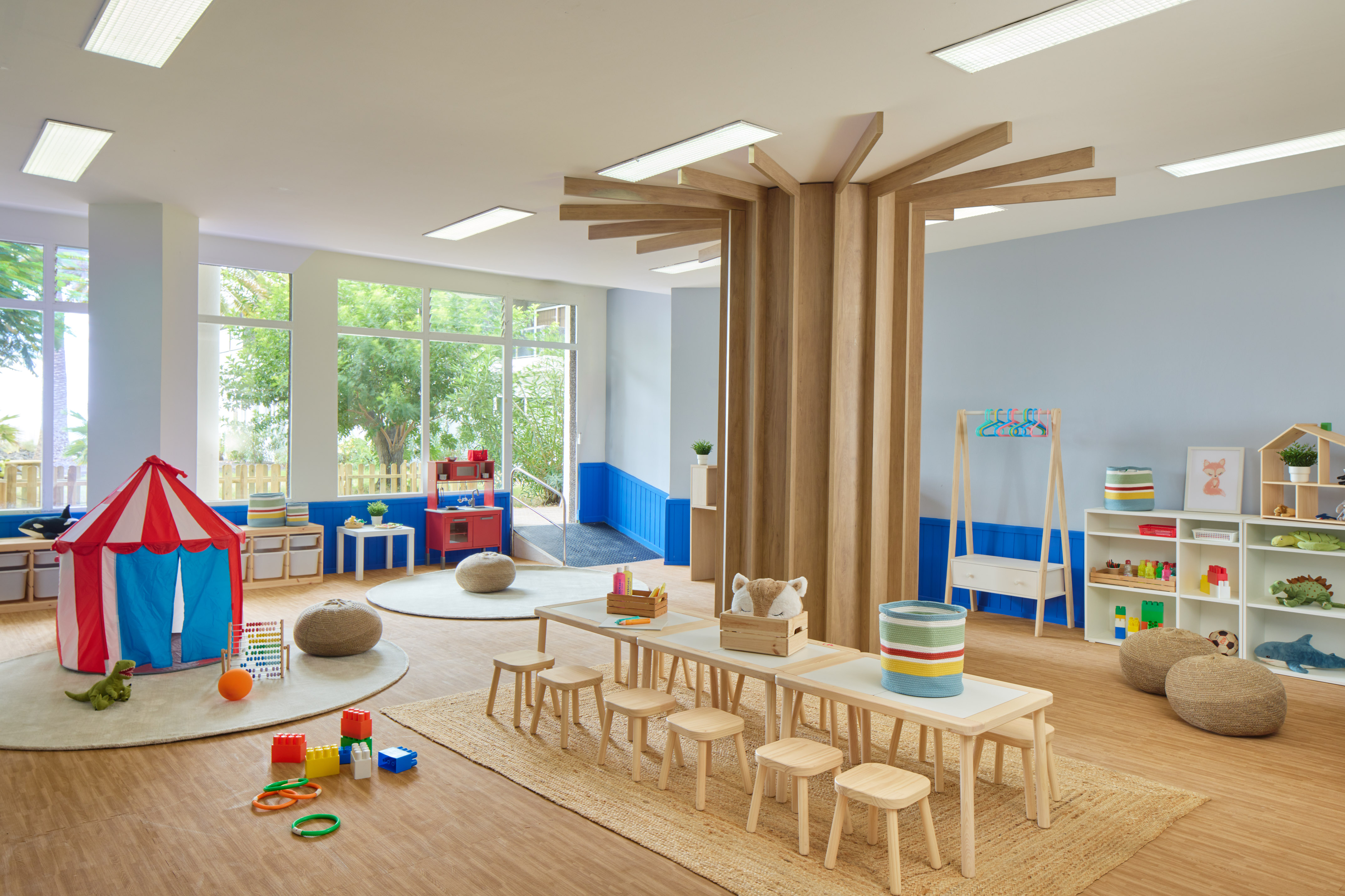 Bright children's playroom with tent, small tables, and a wooden tree structure.