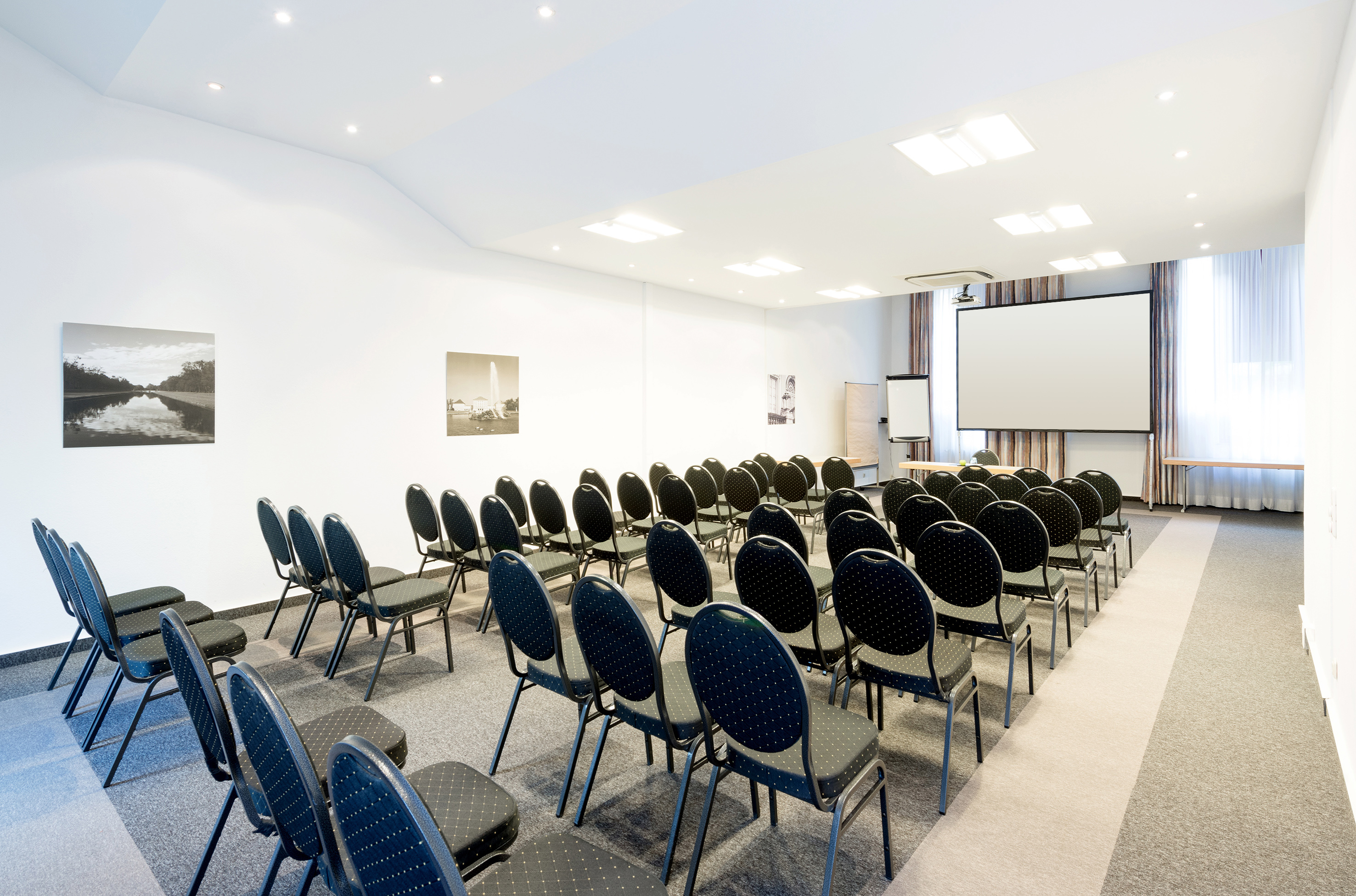 Modern conference room with rows of chairs and a large projection screen.