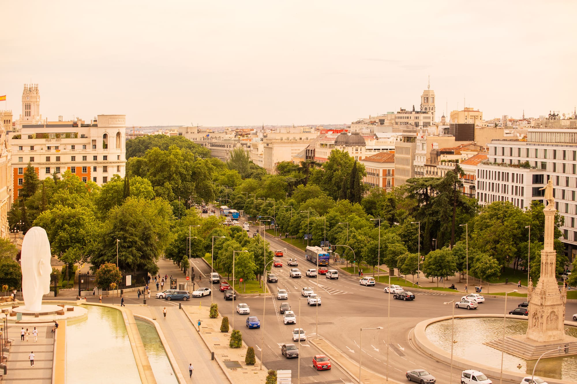 Madrid: Busy avenue, green trees, Plaza de Colón, Columbus monument, modern sculpture.