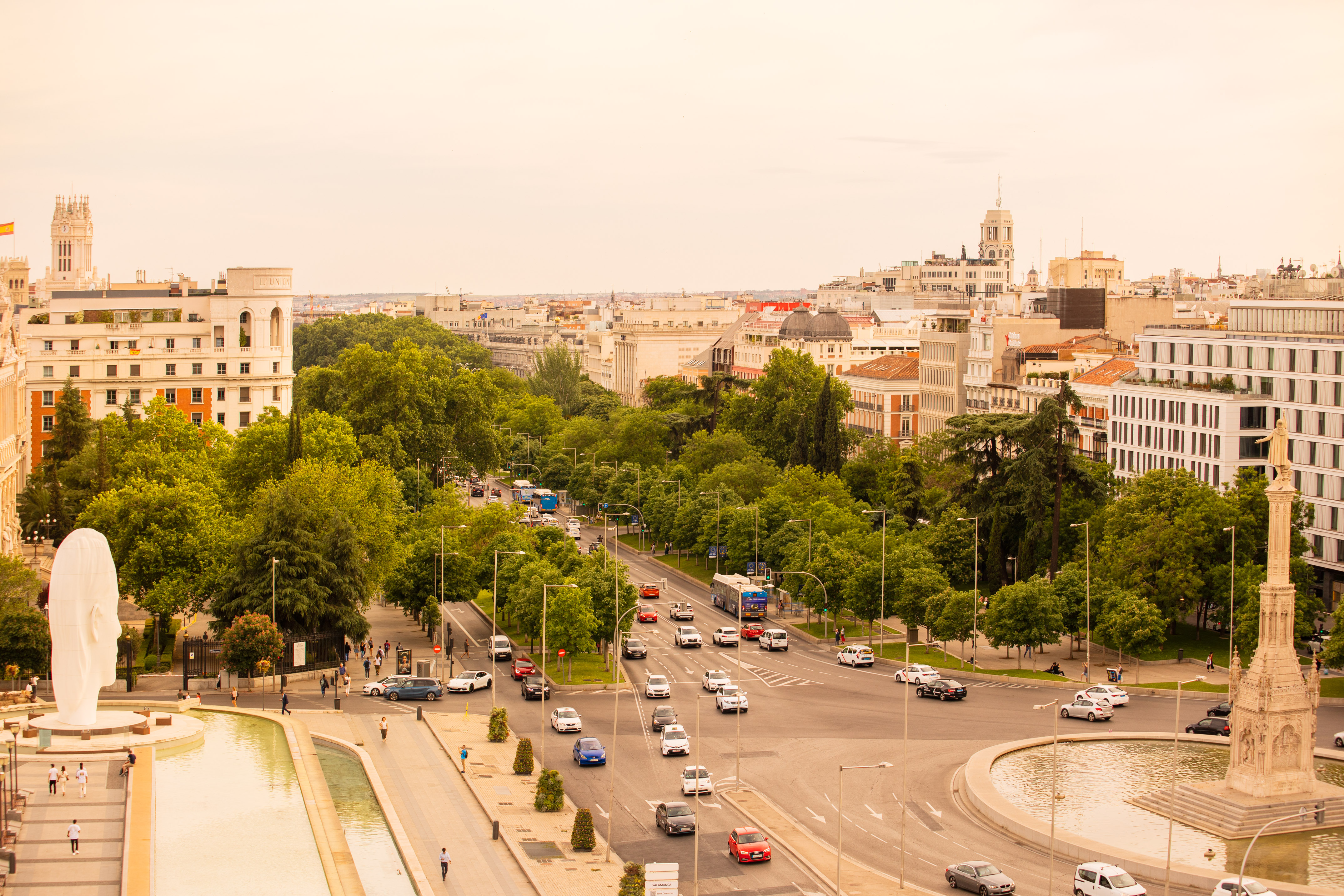Madrid: Busy avenue, green trees, Plaza de Colón, Columbus monument, modern sculpture.
