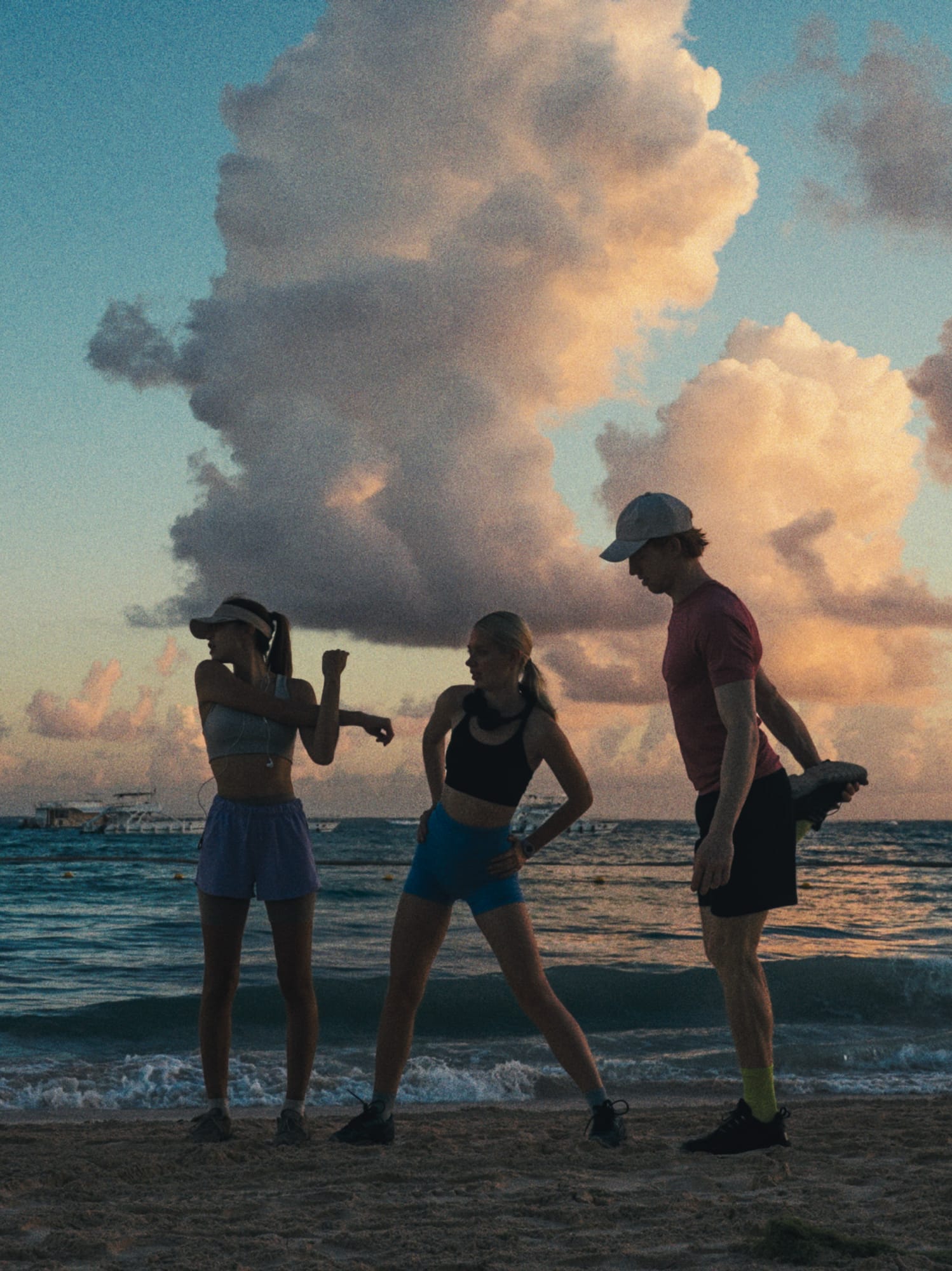 Tres amigos estirando en la playa al atardecer, océano y nubes. Grupo fitness.