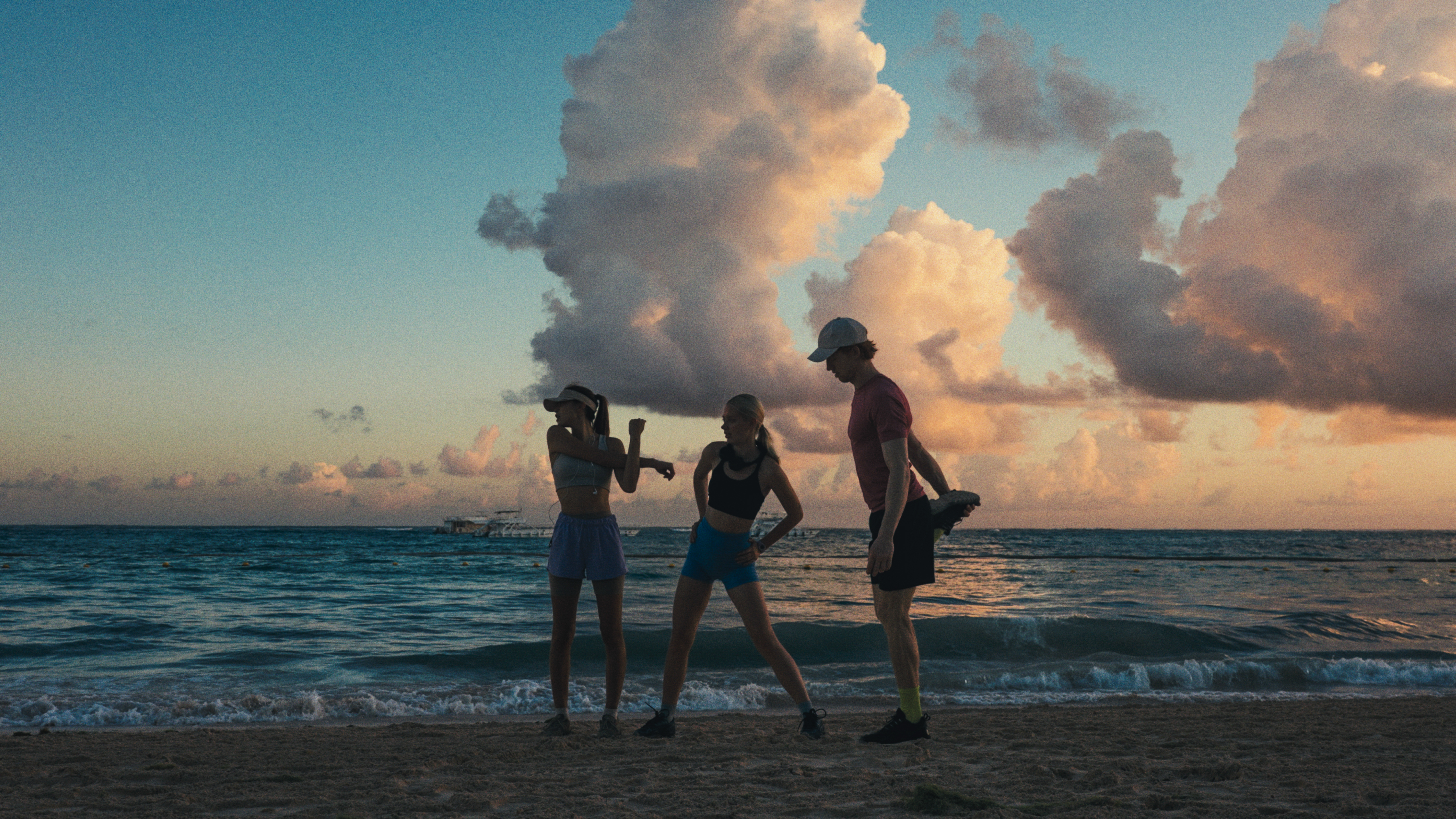 Tres amigos estirando en la playa al atardecer, océano y nubes. Grupo fitness.