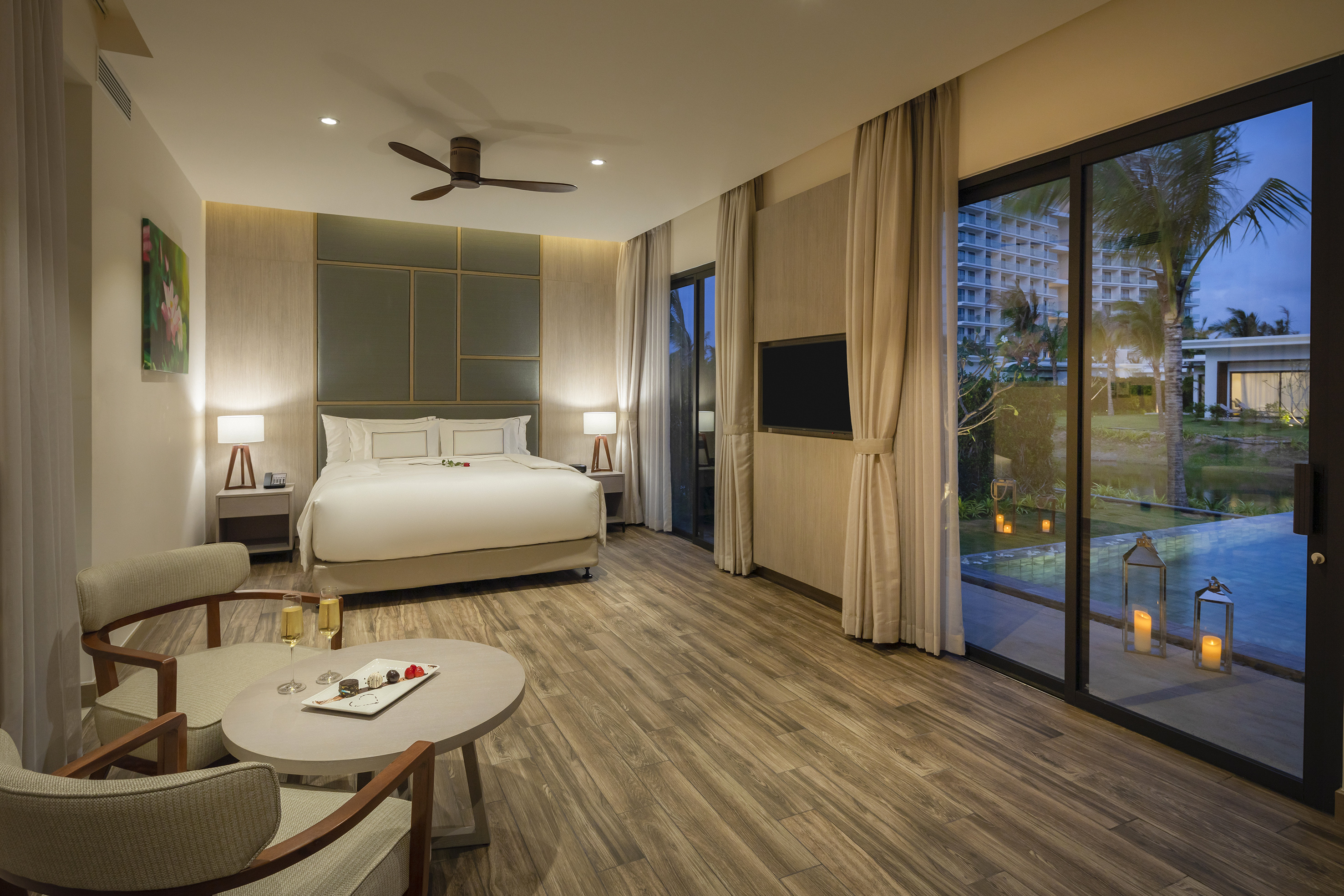 Luxury resort suite with king bed, evening pool view, patio, and champagne.