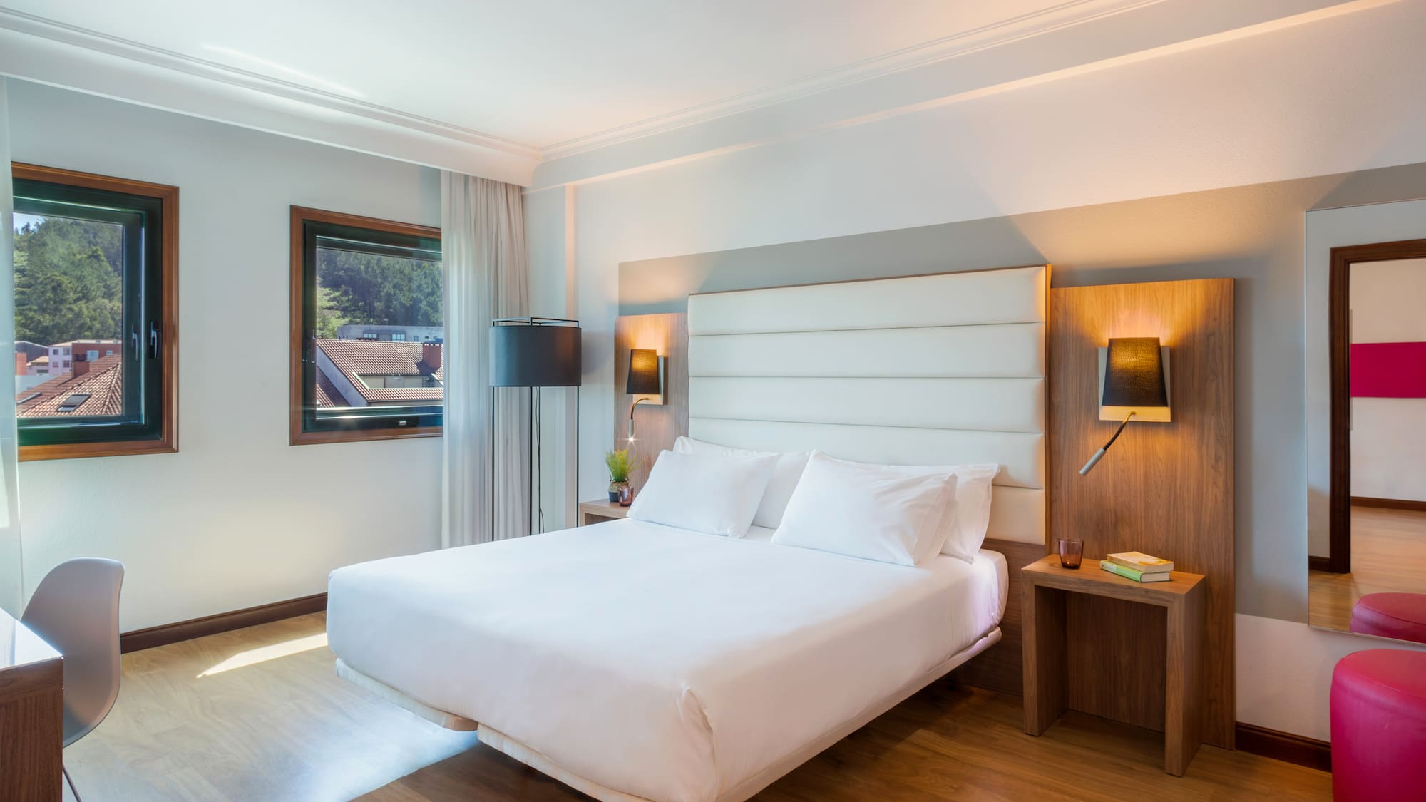 Bright modern hotel bedroom with queen bed, wood floor, and two windows.