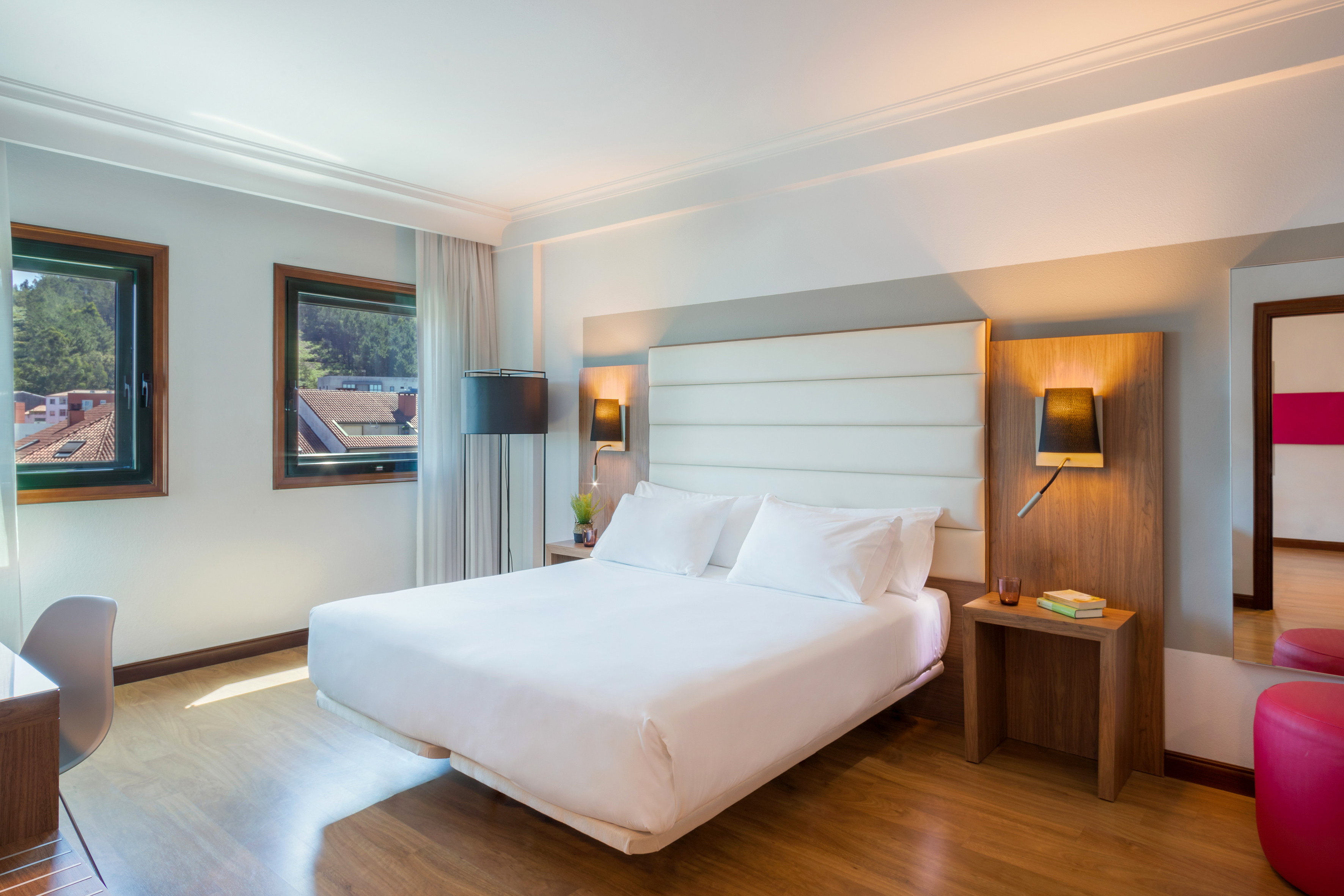 Bright modern hotel bedroom with queen bed, wood floor, and two windows.