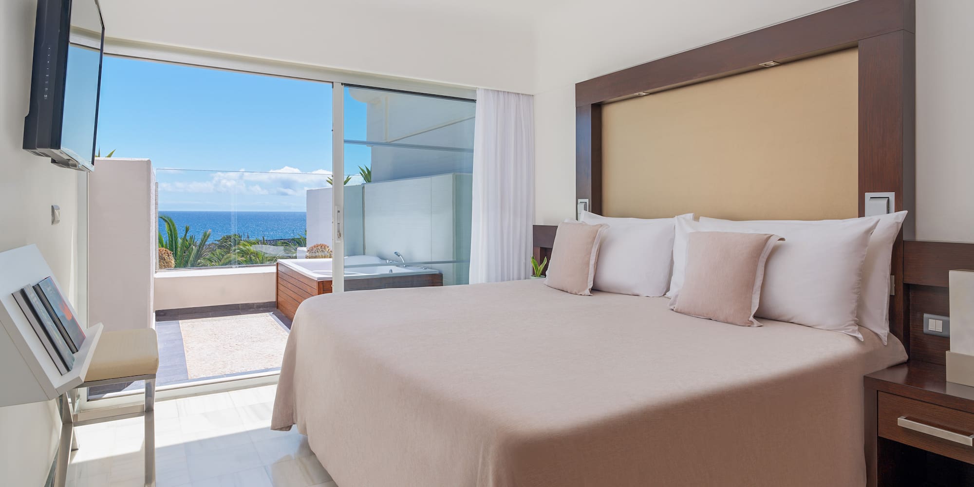 Modern bedroom with ocean view balcony, jacuzzi, and king bed.
