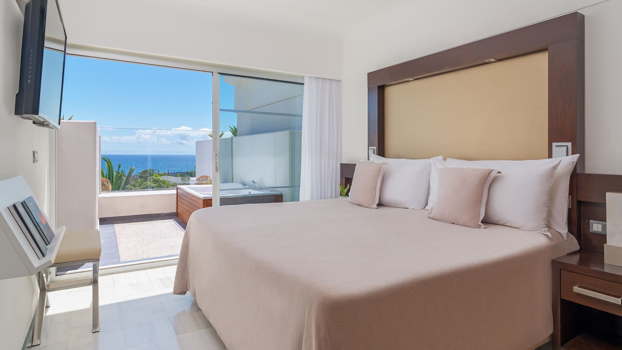 Modern bedroom with ocean view balcony, jacuzzi, and king bed.