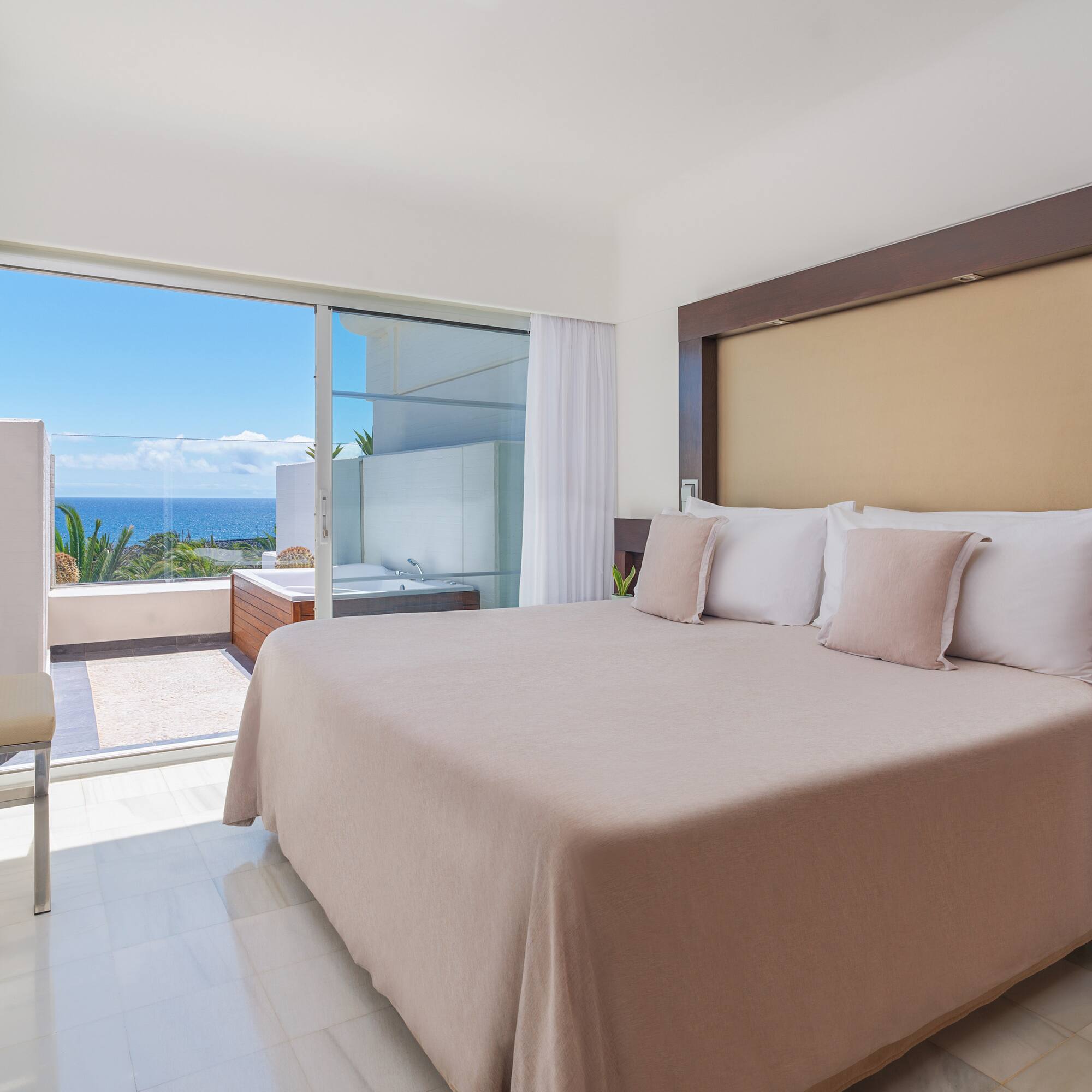 Modern bedroom with ocean view balcony, jacuzzi, and king bed.