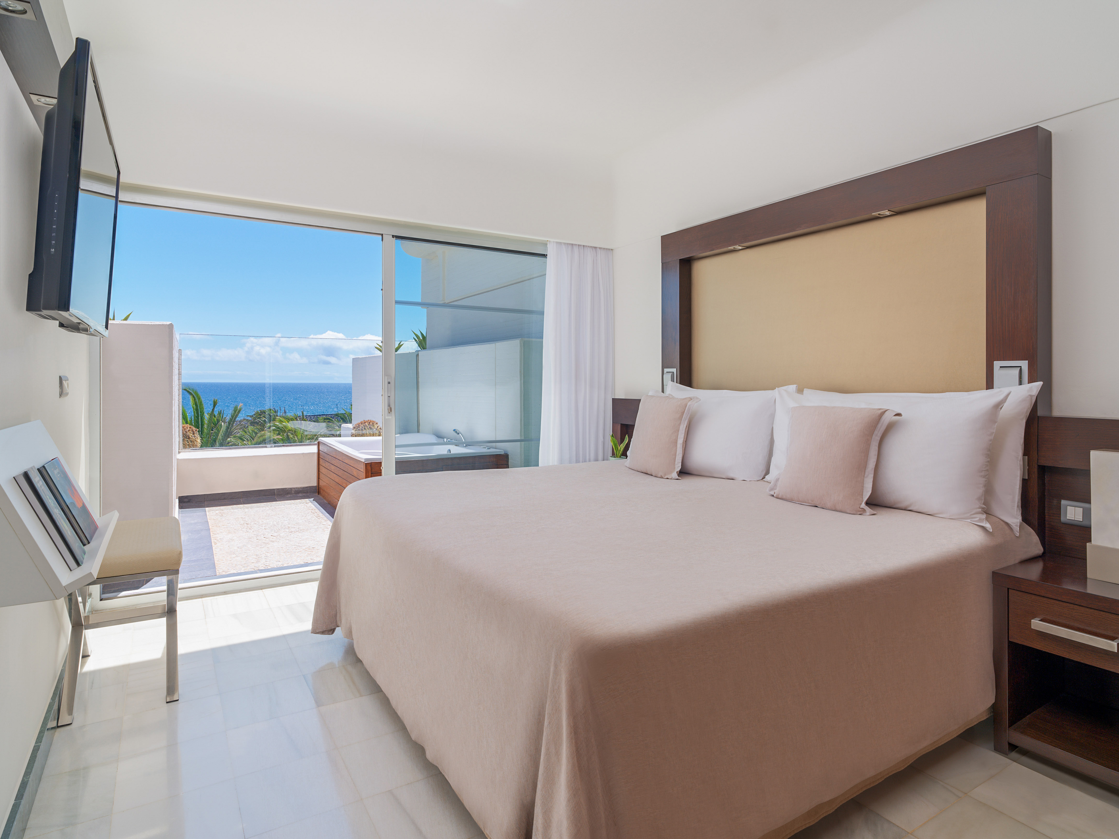 Modern bedroom with ocean view balcony, jacuzzi, and king bed.