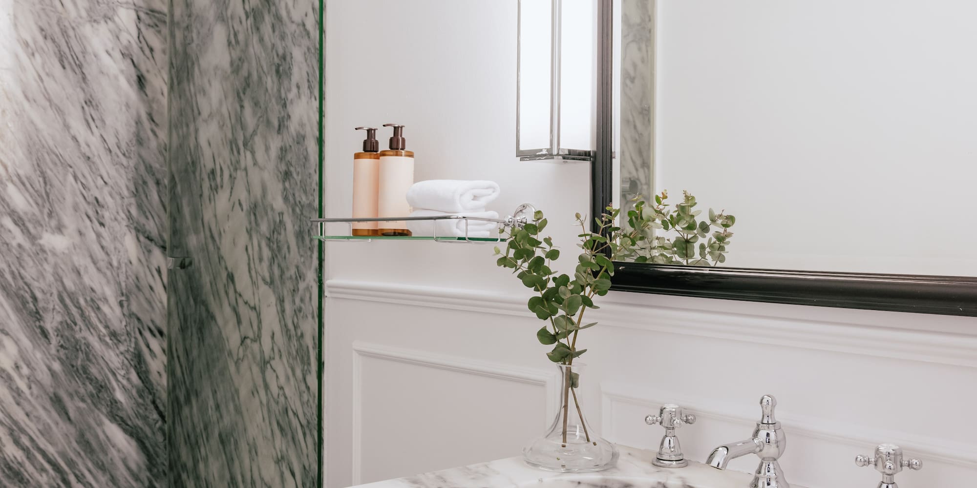 Elegant marble bathroom featuring white vanity, glass shower, and mirror.