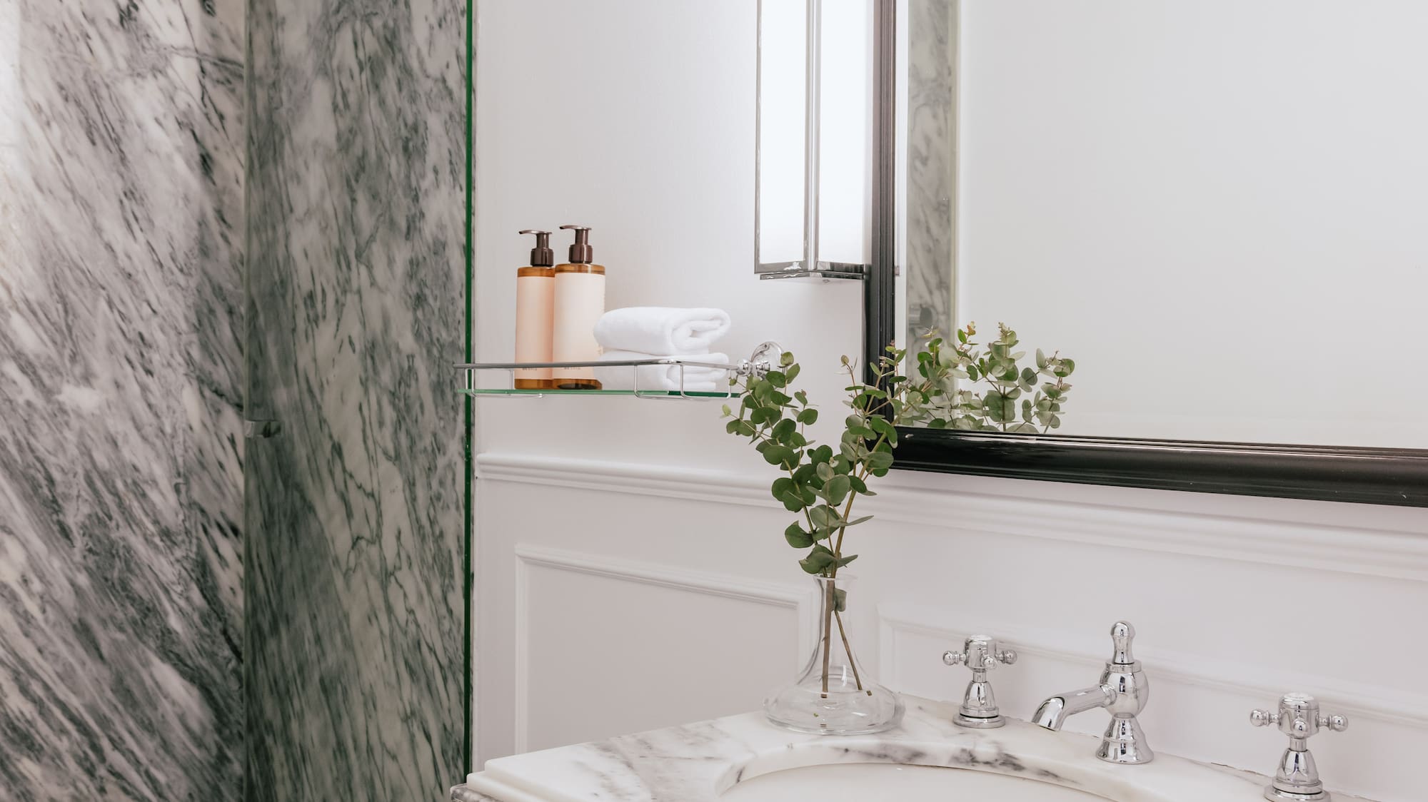 Luxury bathroom with marble shower, white vanity, mirror, and chrome faucet.