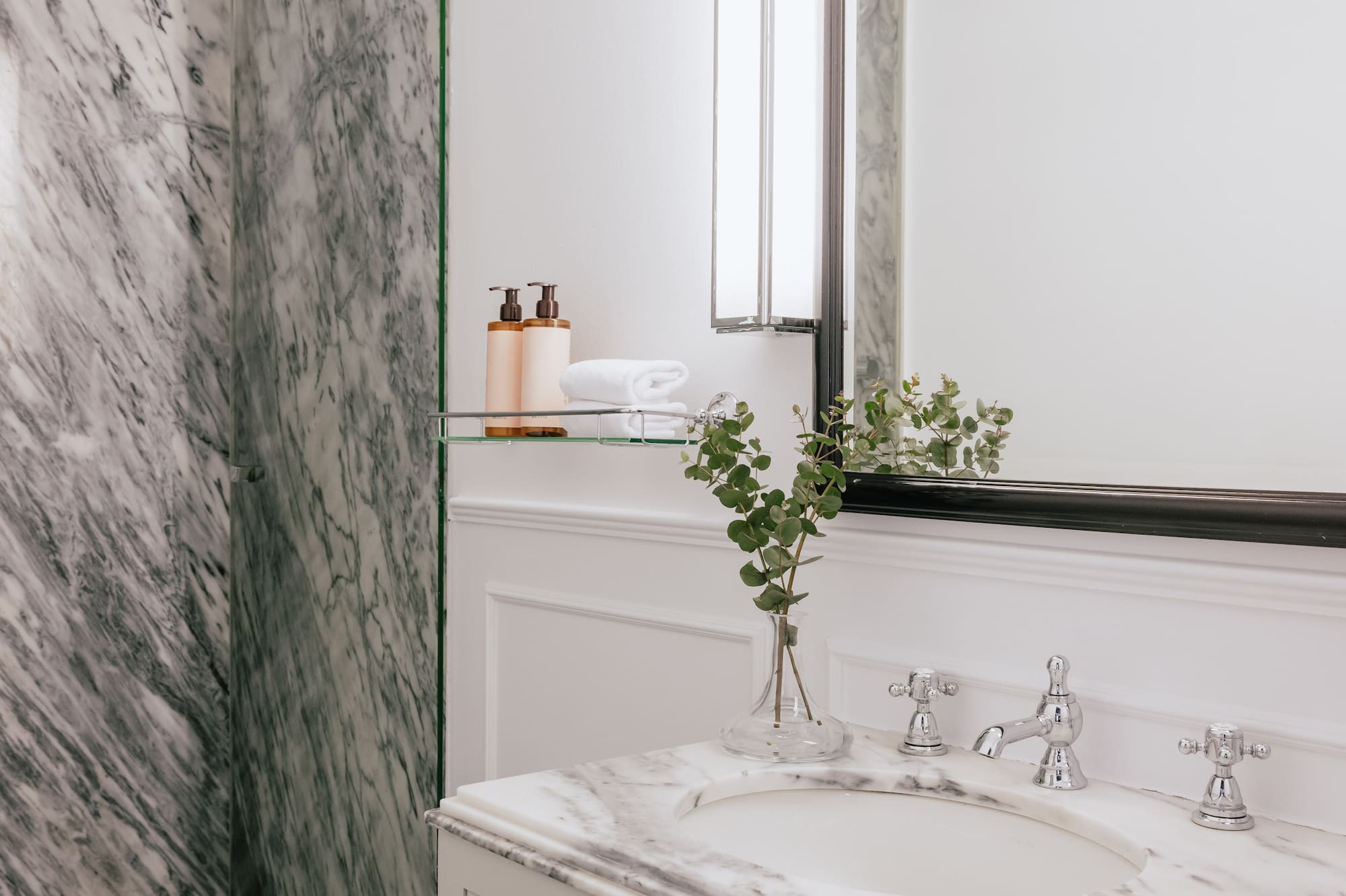 Elegant marble bathroom featuring white vanity, glass shower, and mirror.