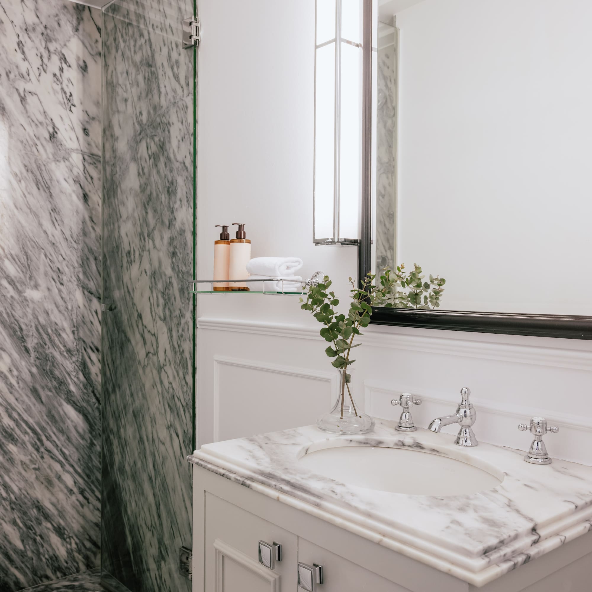 Elegant marble bathroom featuring white vanity, glass shower, and mirror.