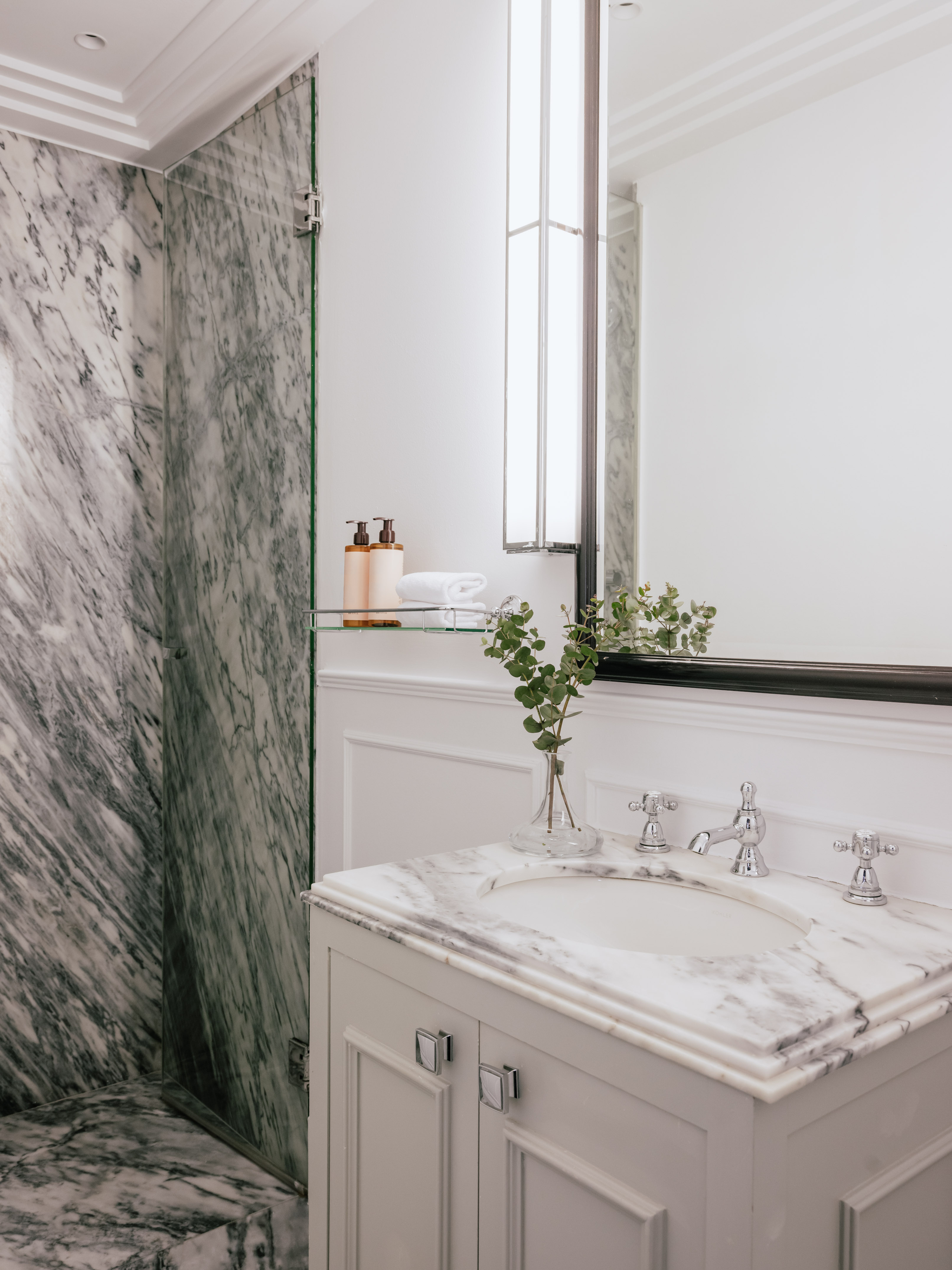 Elegant marble bathroom featuring white vanity, glass shower, and mirror.