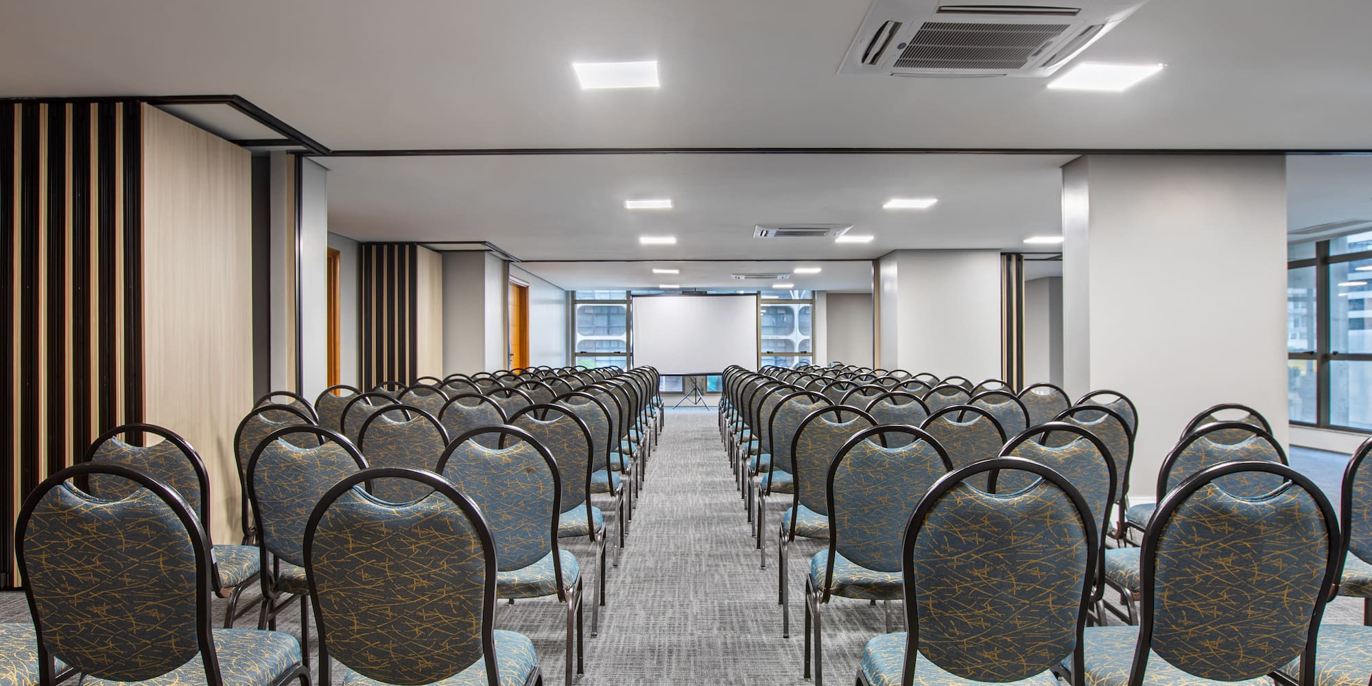 Spacious empty conference room with rows of chairs and a projection screen.