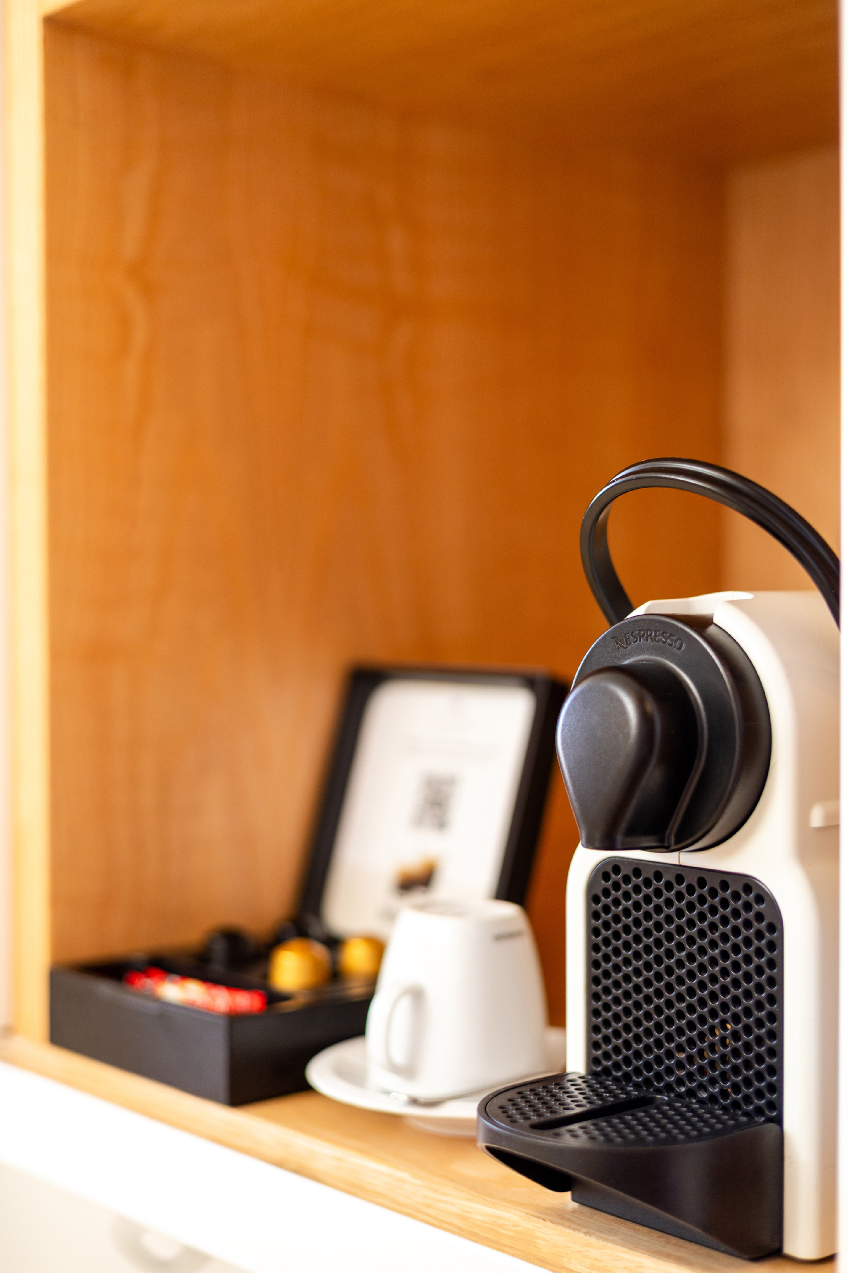 In-room Nespresso coffee machine, pods, and cup on a wooden shelf.