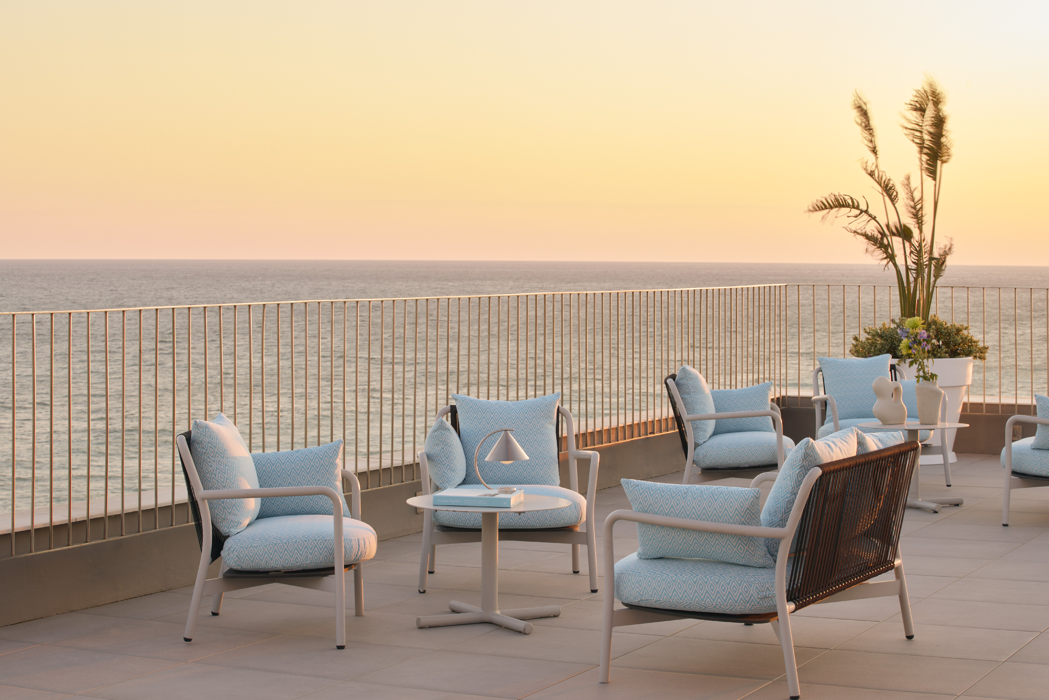 Ocean view terrace with modern patio chairs and blue cushions at sunset.
