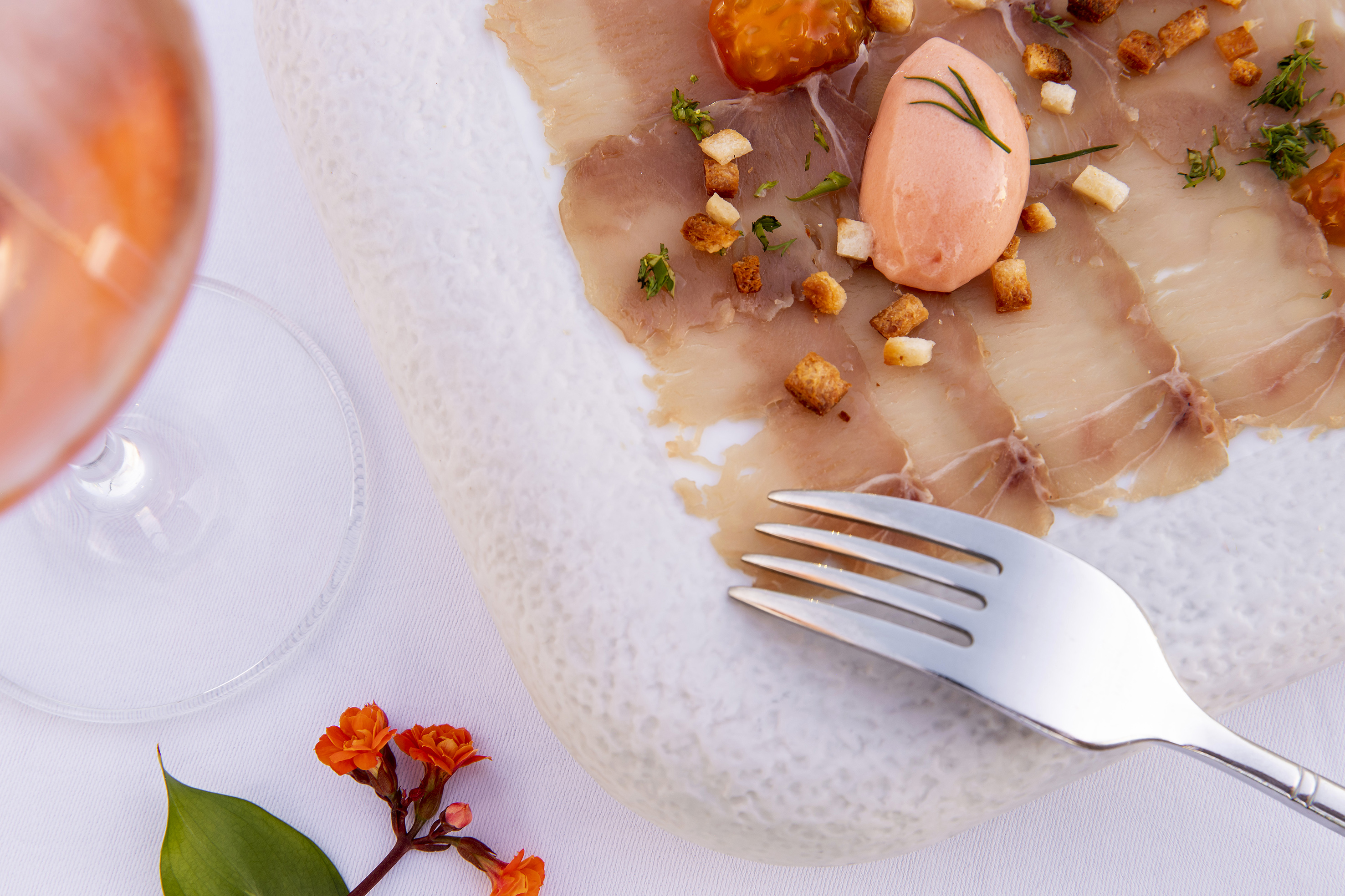 Gourmet carpaccio with pink sorbet, croutons, and herbs, beside a rosé wine.