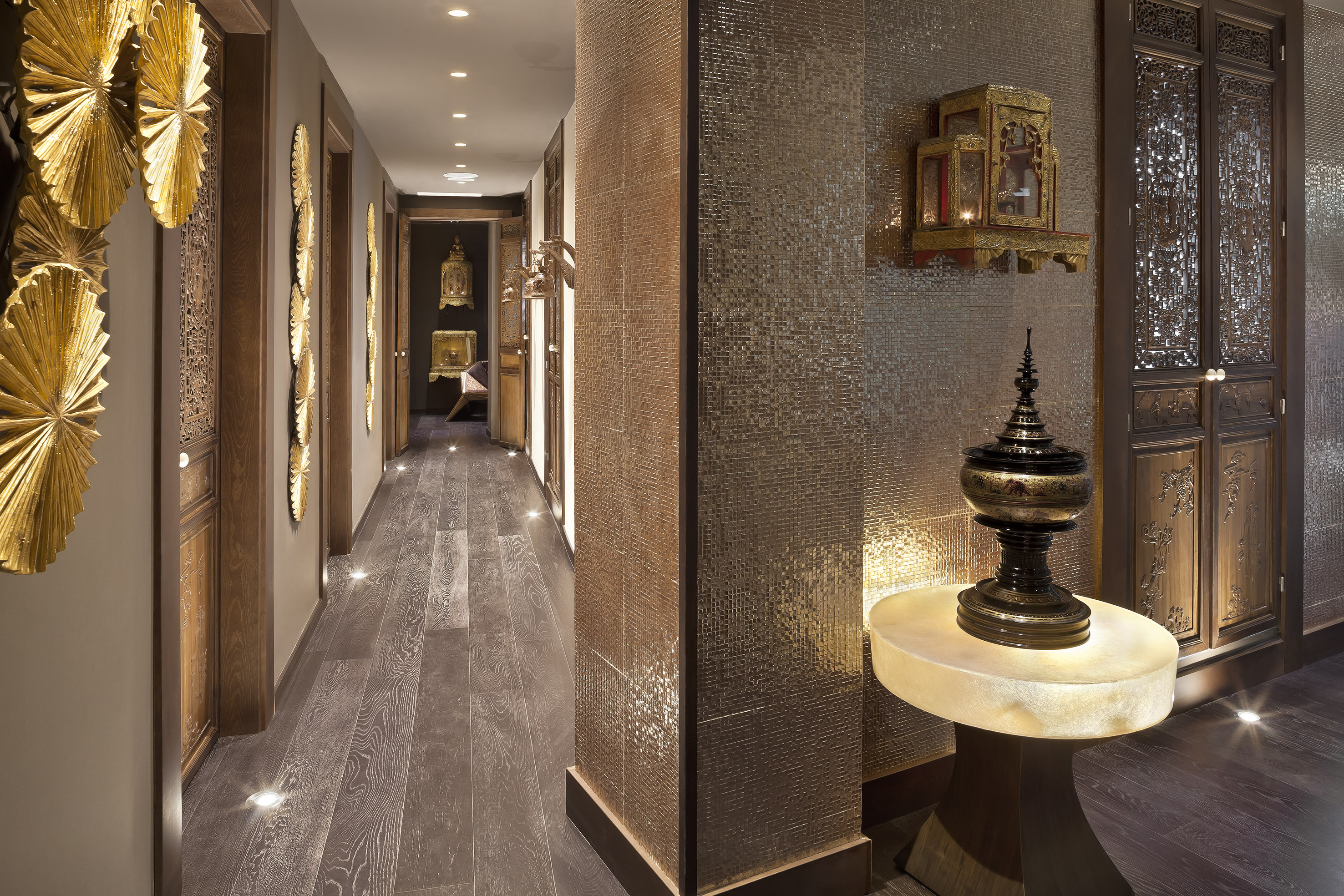 Elegant Asian-inspired hallway with mosaic wall, carved doors, gold fan decor.
