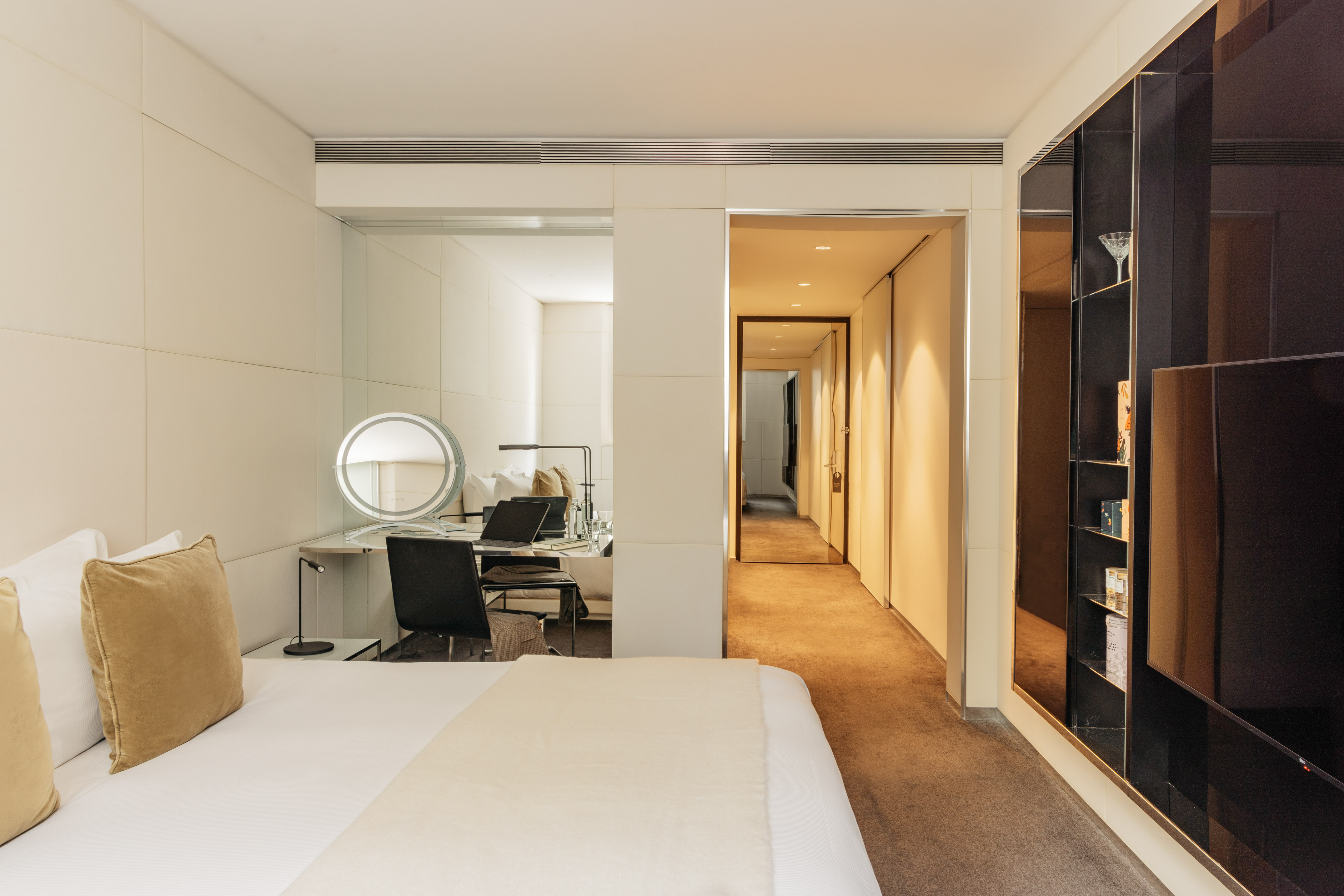 Luxury hotel room interior with bed, desk, vanity mirror, and elegant hallway.