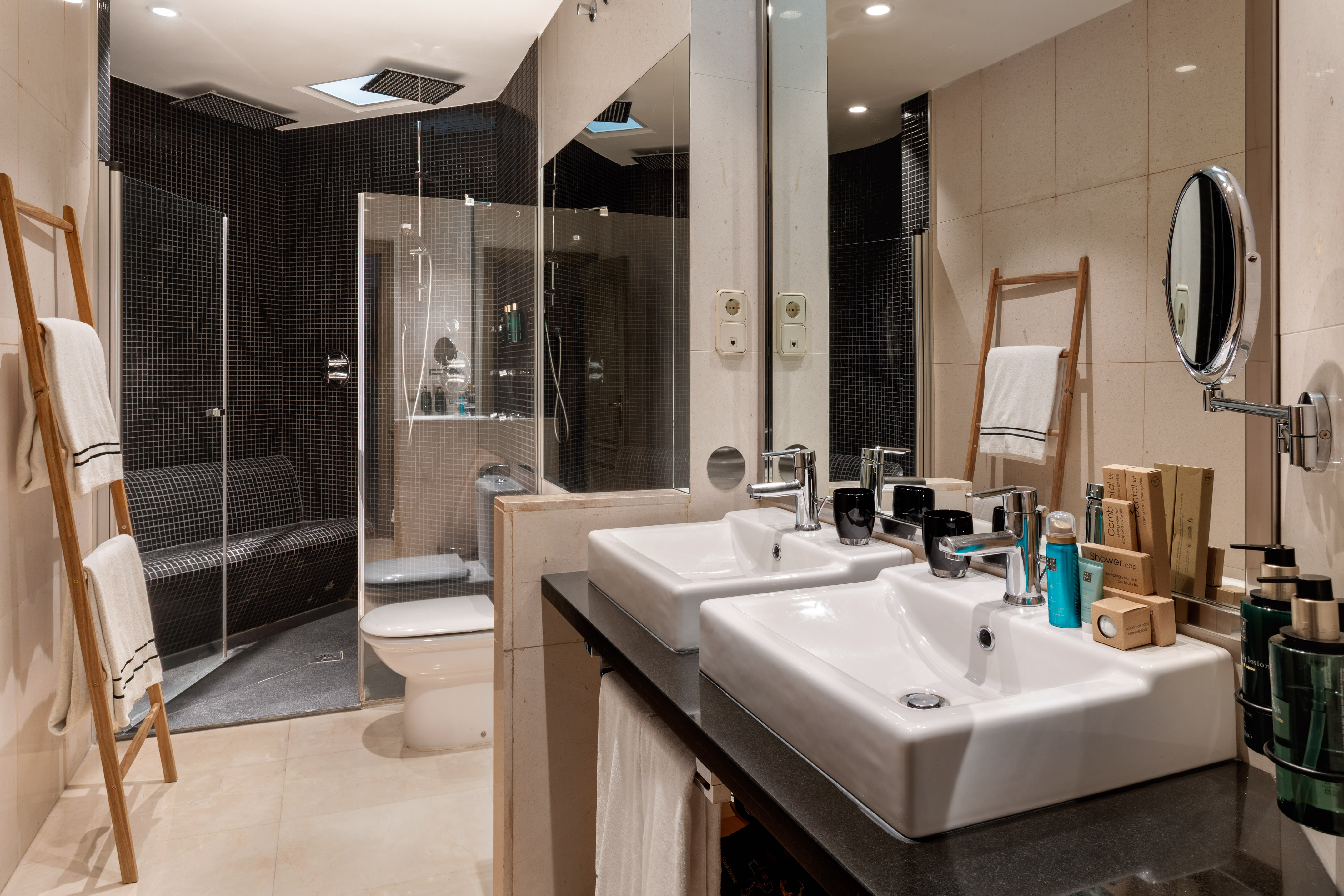 Modern hotel bathroom with dual vanity sinks and black tiled steam shower.