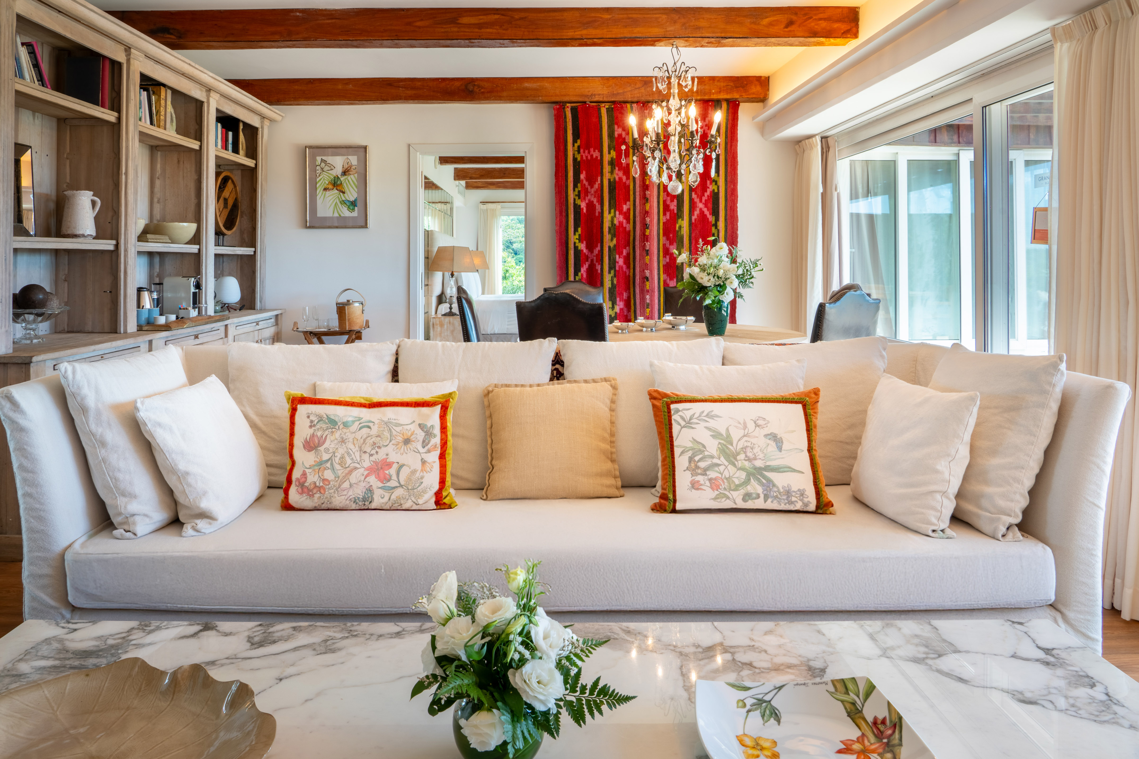 Luxury living room with white sofa, marble table, wood beams, and dining space.