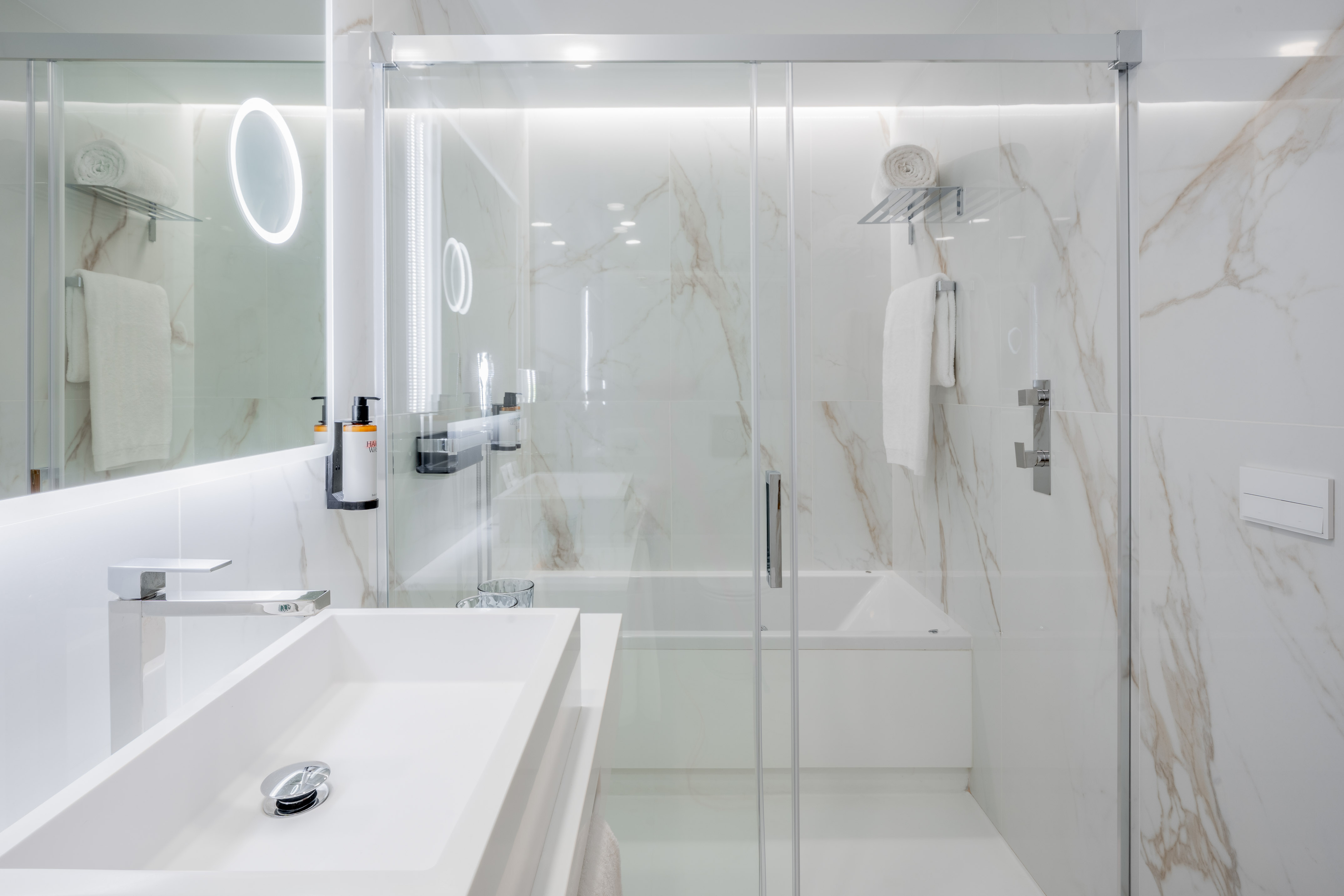 Modern white marble bathroom with walk-in shower, bathtub, and vanity.